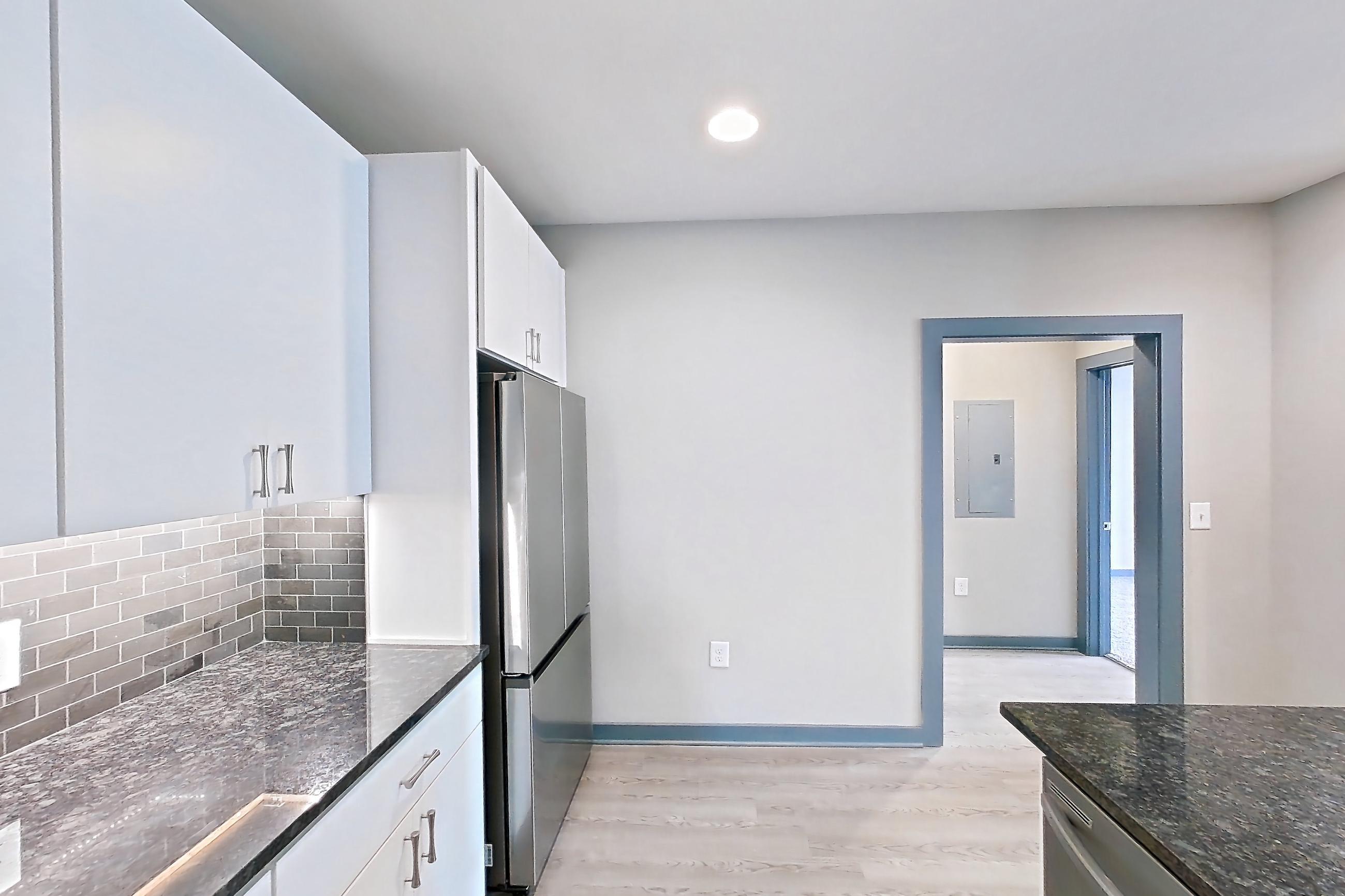 Kitchen with black appliances, dark stone countertops, dishwasher, electric range, kitchen island, light countertops, light wood-finish flooring, microwave, oven/range, refrigerator, and stainless steel appliances, Apartment 2040 at Cortland Westshore