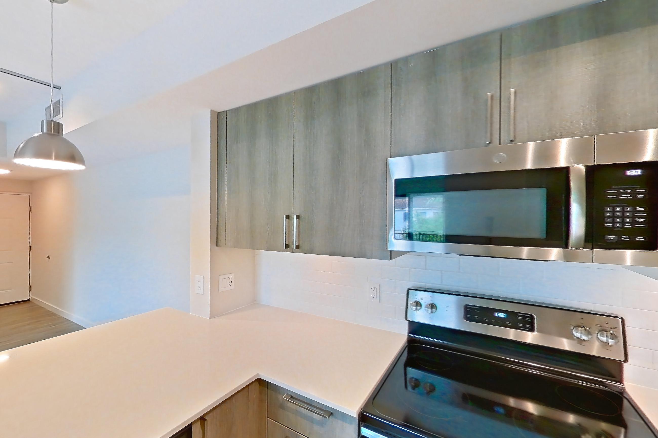 Kitchen with dishwasher, electric range, light countertops, light stone countertops, light wood-finish flooring, microwave, oven/range, and stainless steel appliances, Apartment 08-301 at Cortland South Kendall