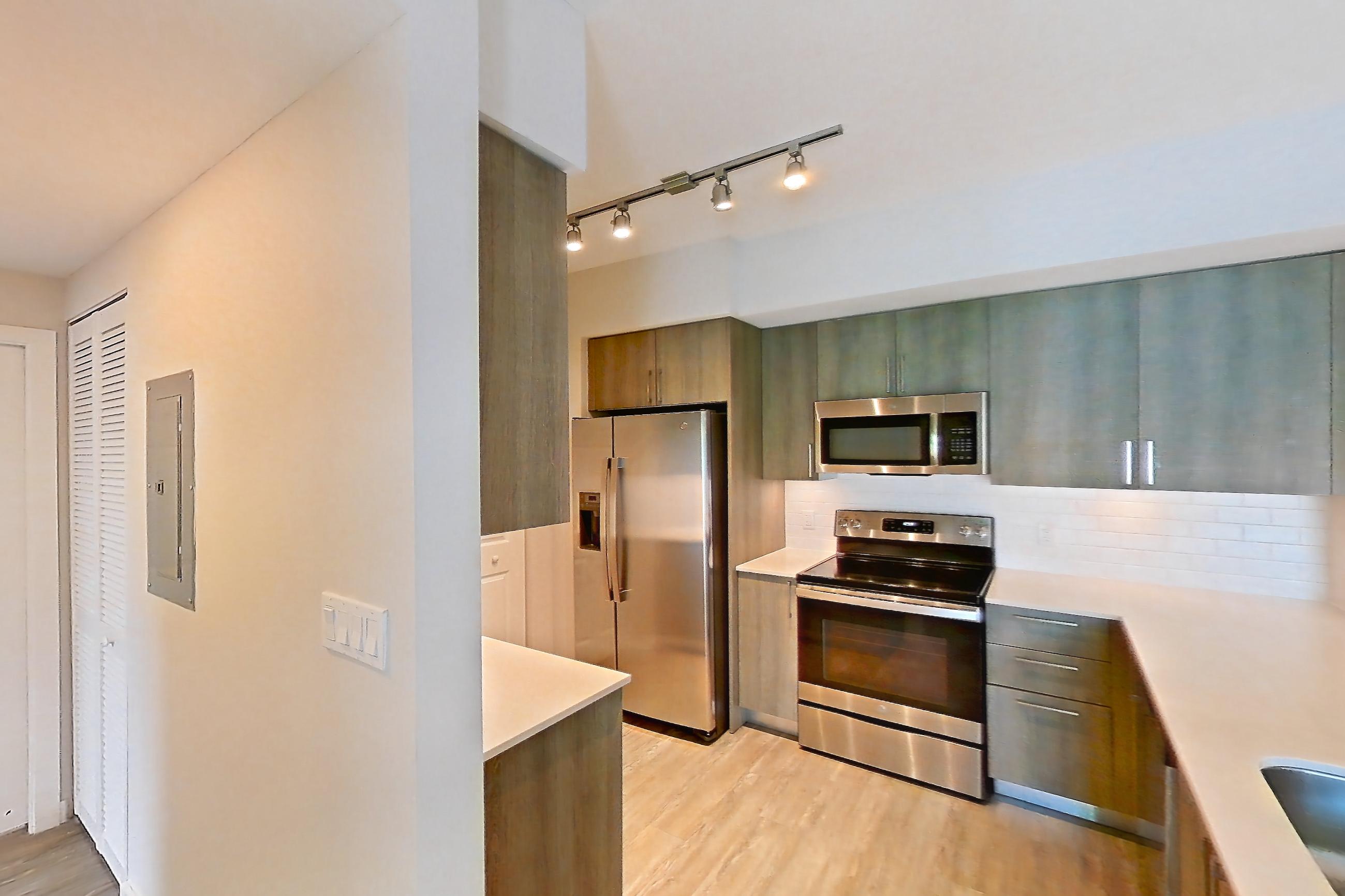 Kitchen entryway with electric range, light countertops, light stone countertops, light wood-finish flooring, oven/range, range hood, refrigerator, stainless steel appliances, and water & ice dispenser, Apartment 08-303 at Cortland South Kendall