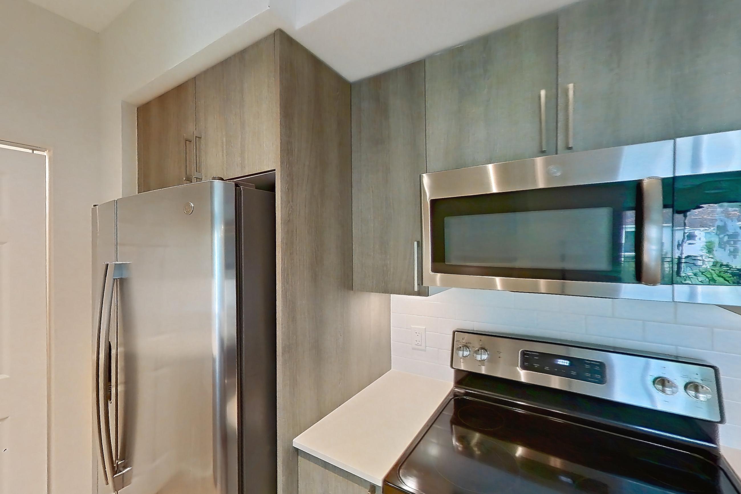 Kitchen with dishwasher, electric range, light countertops, light stone countertops, light wood-finish flooring, microwave, oven/range, refrigerator, and stainless steel appliances, Apartment 08-303 at Cortland South Kendall