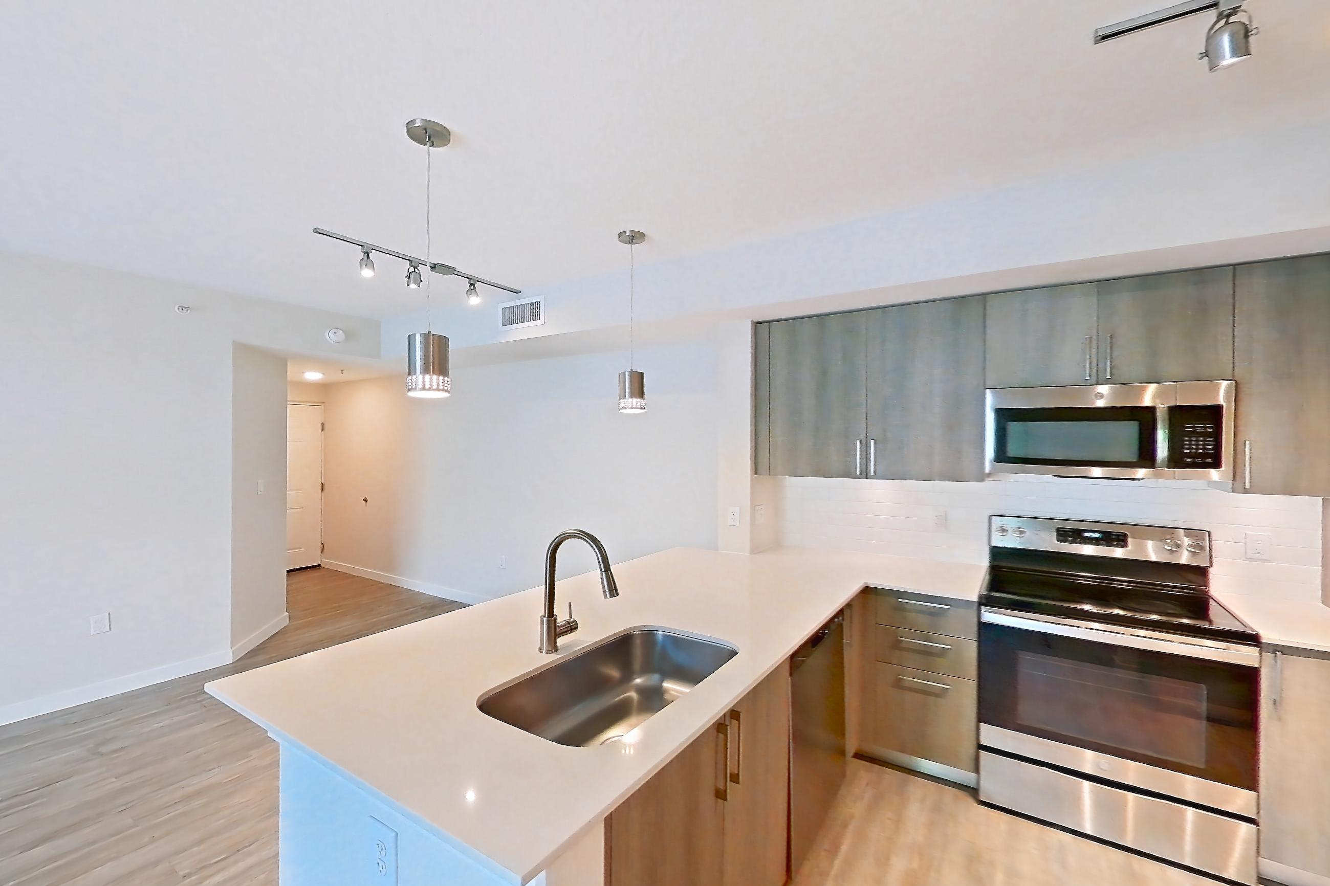 Kitchen entryway with dishwasher, electric range, light stone countertops, light wood-finish flooring, oven/range, refrigerator, stainless steel appliances, and water & ice dispenser, Apartment 08-201 at Cortland South Kendall