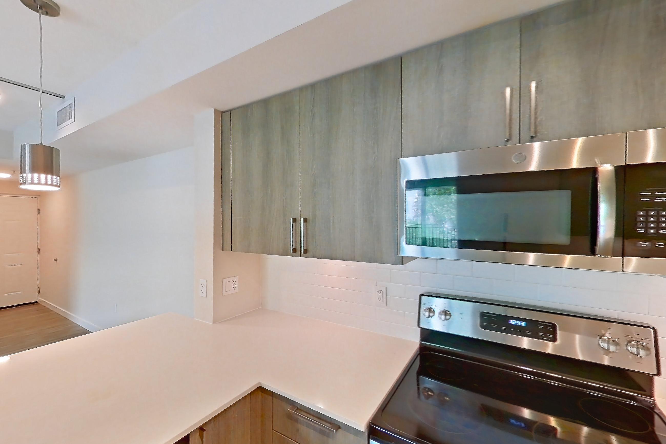 Kitchen with dishwasher, electric range, light countertops, light stone countertops, light wood-finish flooring, microwave, oven/range, and stainless steel appliances, Apartment 08-201 at Cortland South Kendall
