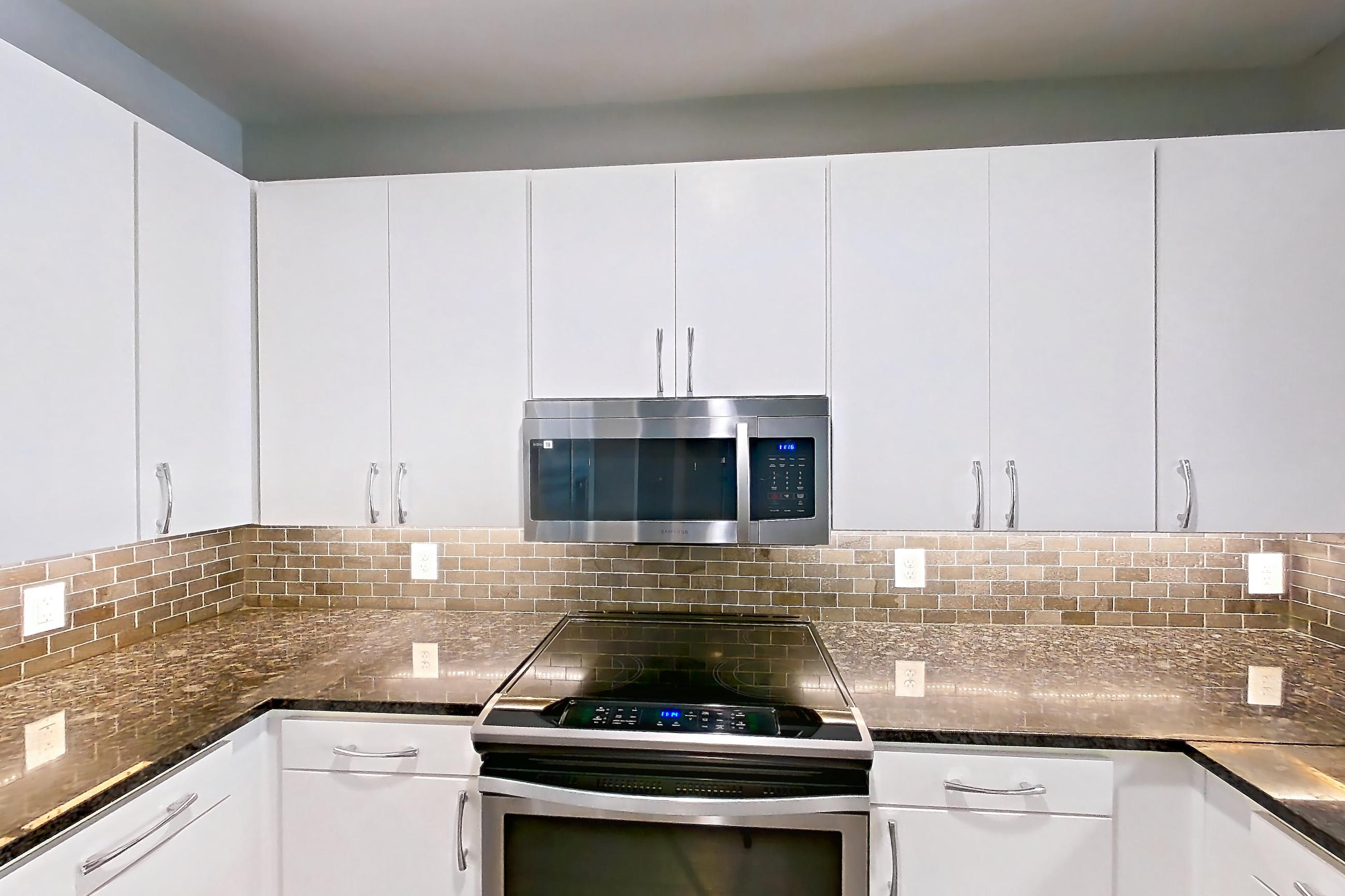 Kitchen with dark stone countertops, dishwasher, electric range, light countertops, light wood-finish flooring, microwave, oven/range, refrigerator, stainless steel appliances, water & ice dispenser, and white appliances, Apartment 6017 at Cortland Westshore