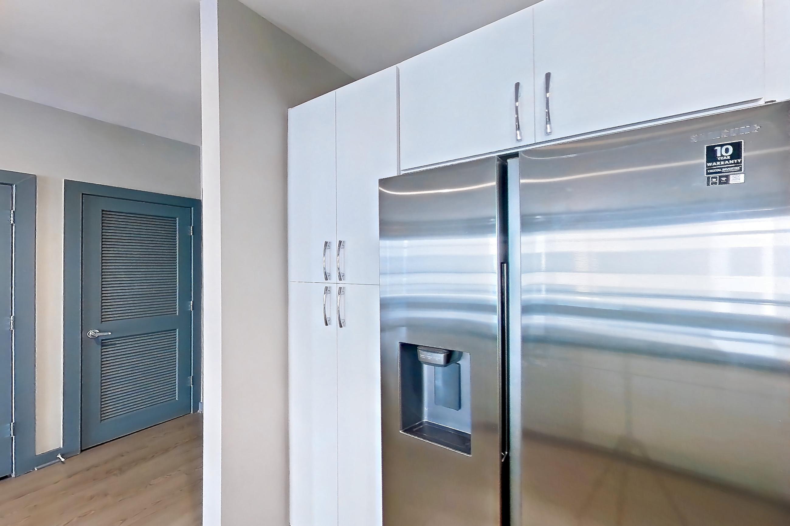 Kitchen with dark stone countertops, dishwasher, electric range, light countertops, light wood-finish flooring, microwave, oven/range, refrigerator, stainless steel appliances, water & ice dispenser, and white appliances, Apartment 6017 at Cortland Westshore