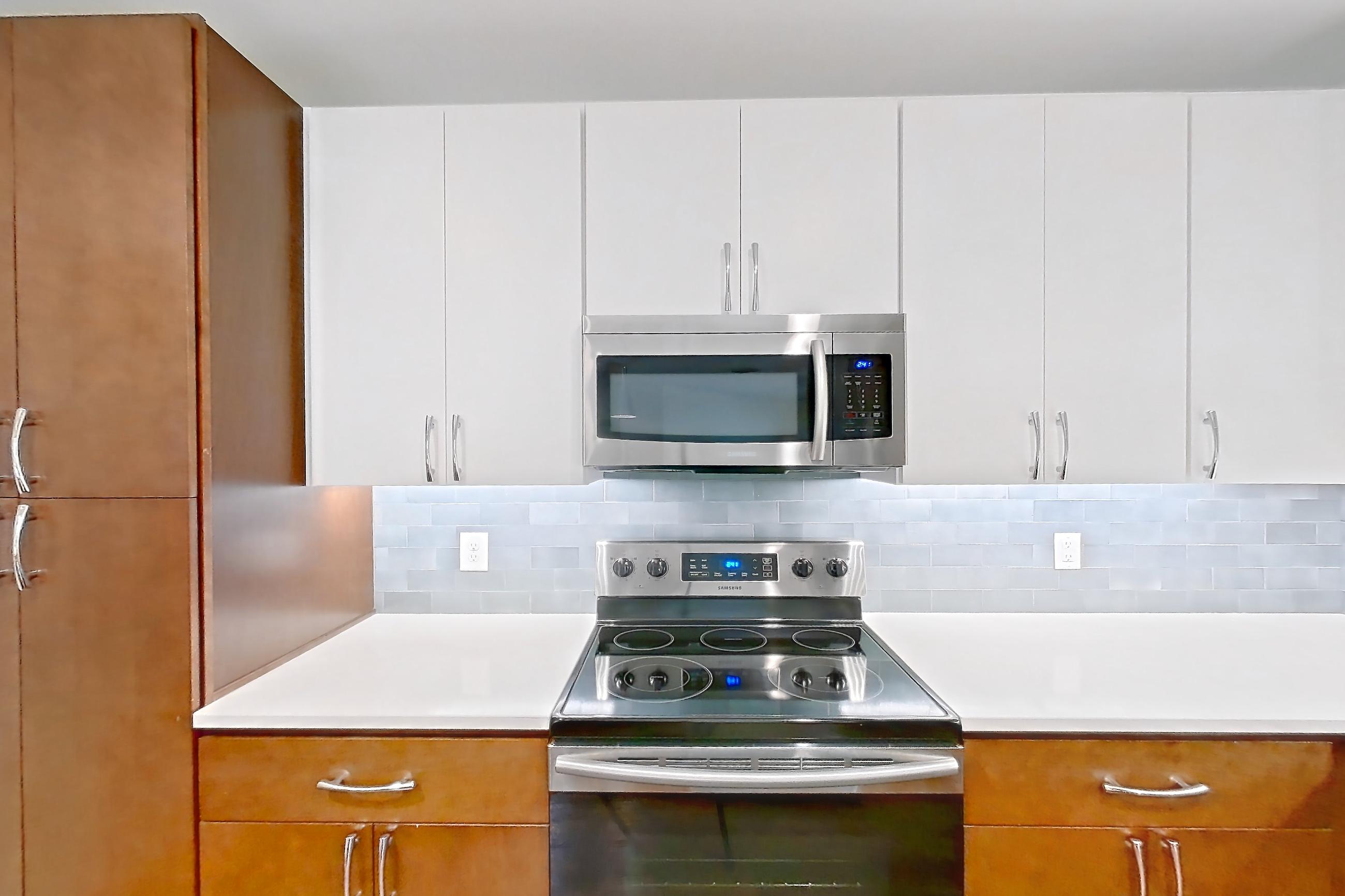 Kitchen with dark wood-finish flooring, dishwasher, electric range, light countertops, light wood-finish flooring, microwave, oven/range, refrigerator, and stainless steel appliances, Apartment 1015 at Cortland Westshore