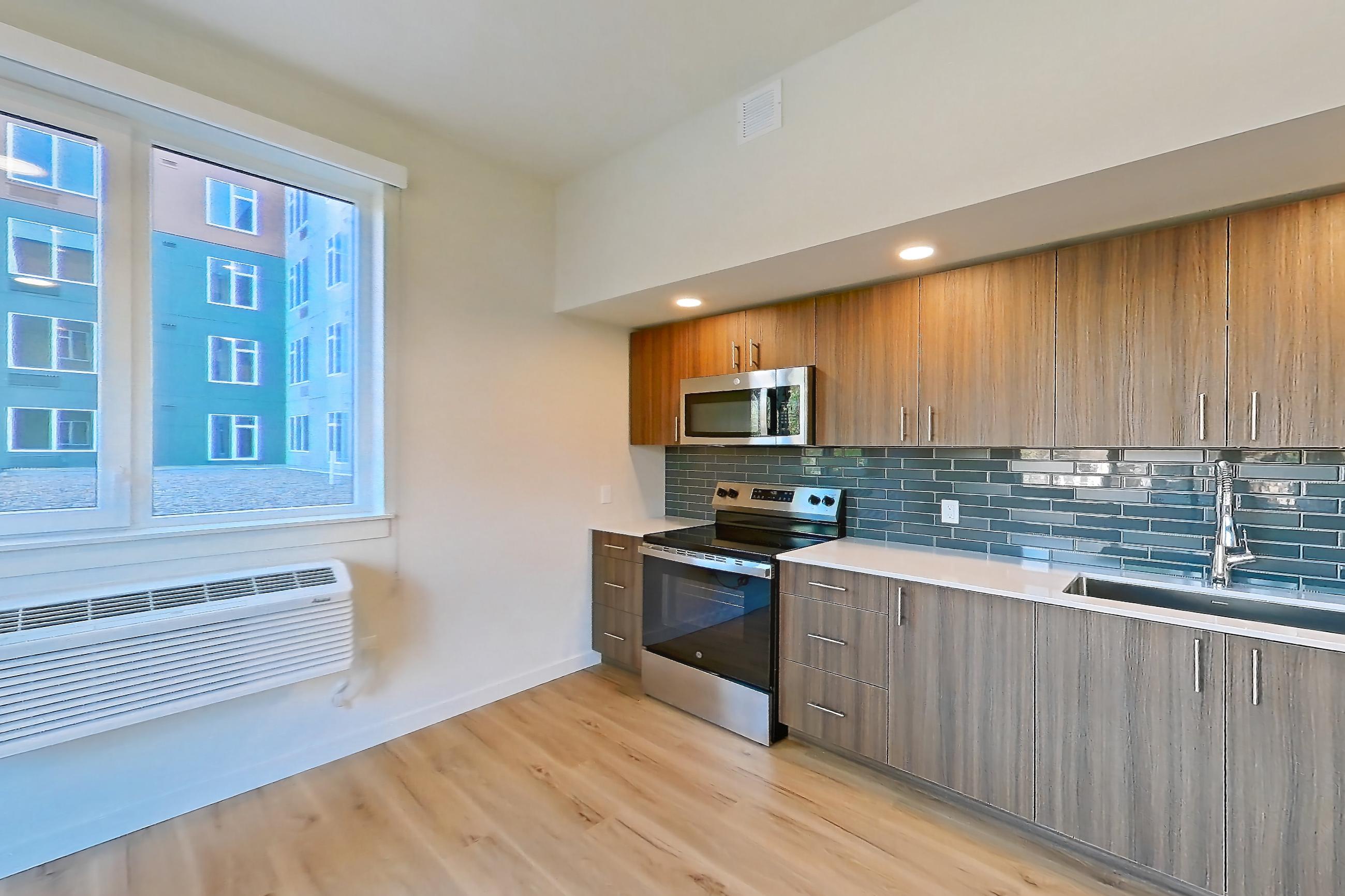 Living room with electric range, light countertops, light wood-finish flooring, microwave, oven/range, and stainless steel appliances, Apartment 307 at Montage Tigard