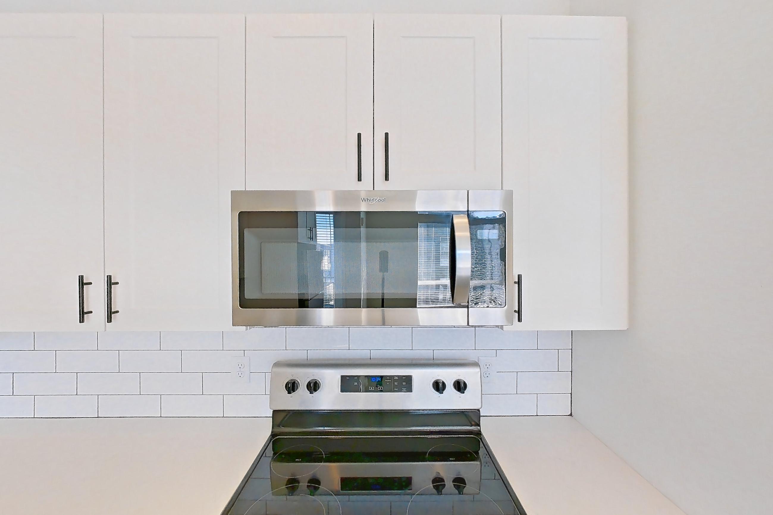 Kitchen with dishwasher, electric range, light countertops, light stone countertops, light wood-finish flooring, microwave, oven/range, and stainless steel appliances, Apartment 10-307 at Marlon at Central Park