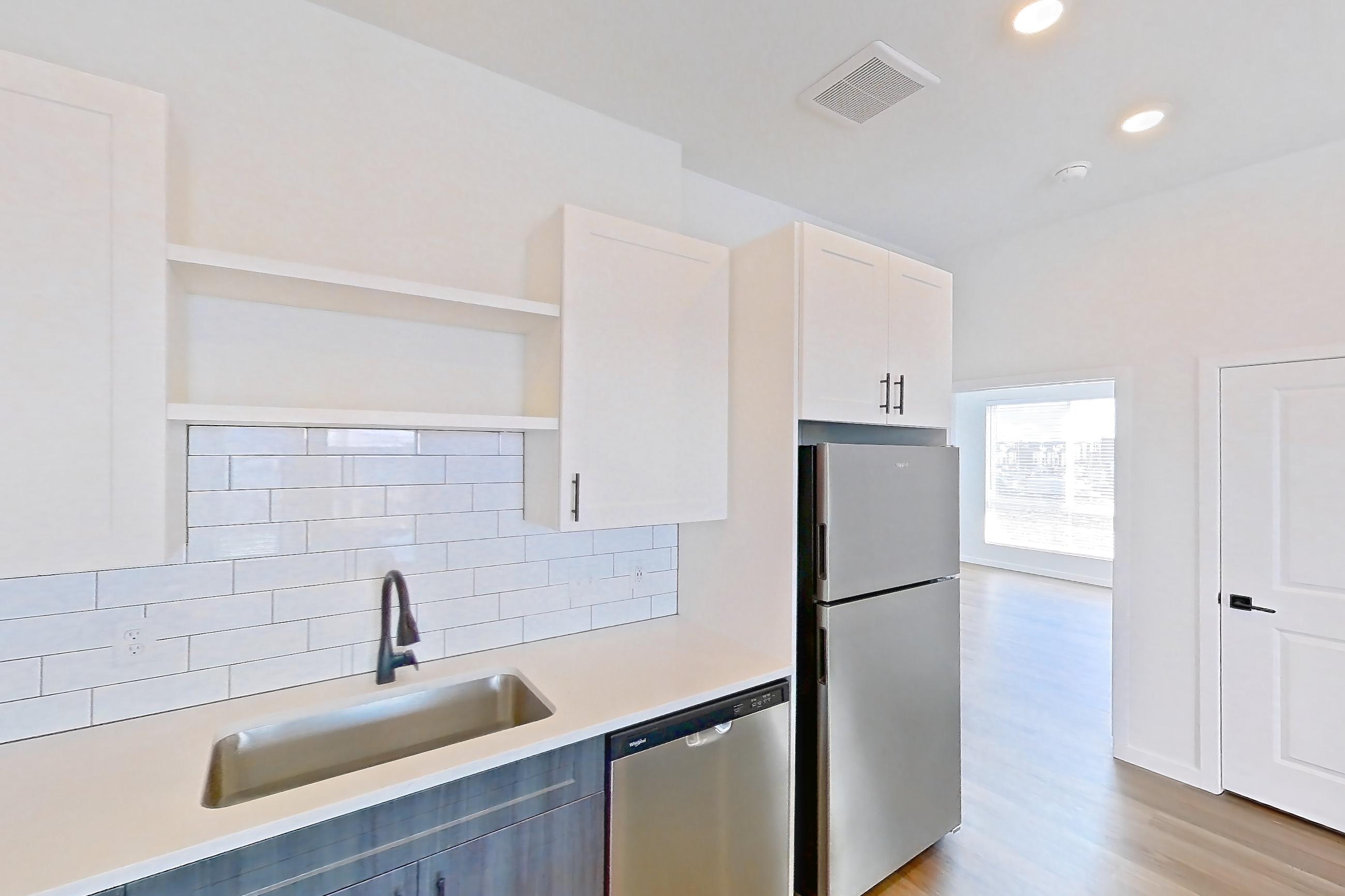 Kitchen with dishwasher, electric range, light countertops, light stone countertops, light wood-finish flooring, microwave, oven/range, and stainless steel appliances, Apartment 06-302 at Marlon at Central Park