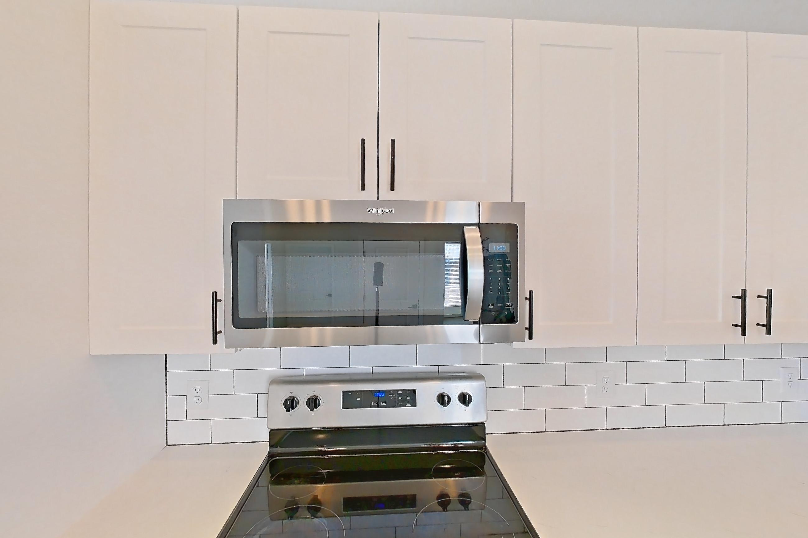 Kitchen with dishwasher, electric range, light countertops, light stone countertops, light wood-finish flooring, microwave, oven/range, and stainless steel appliances, Apartment 06-302 at Marlon at Central Park