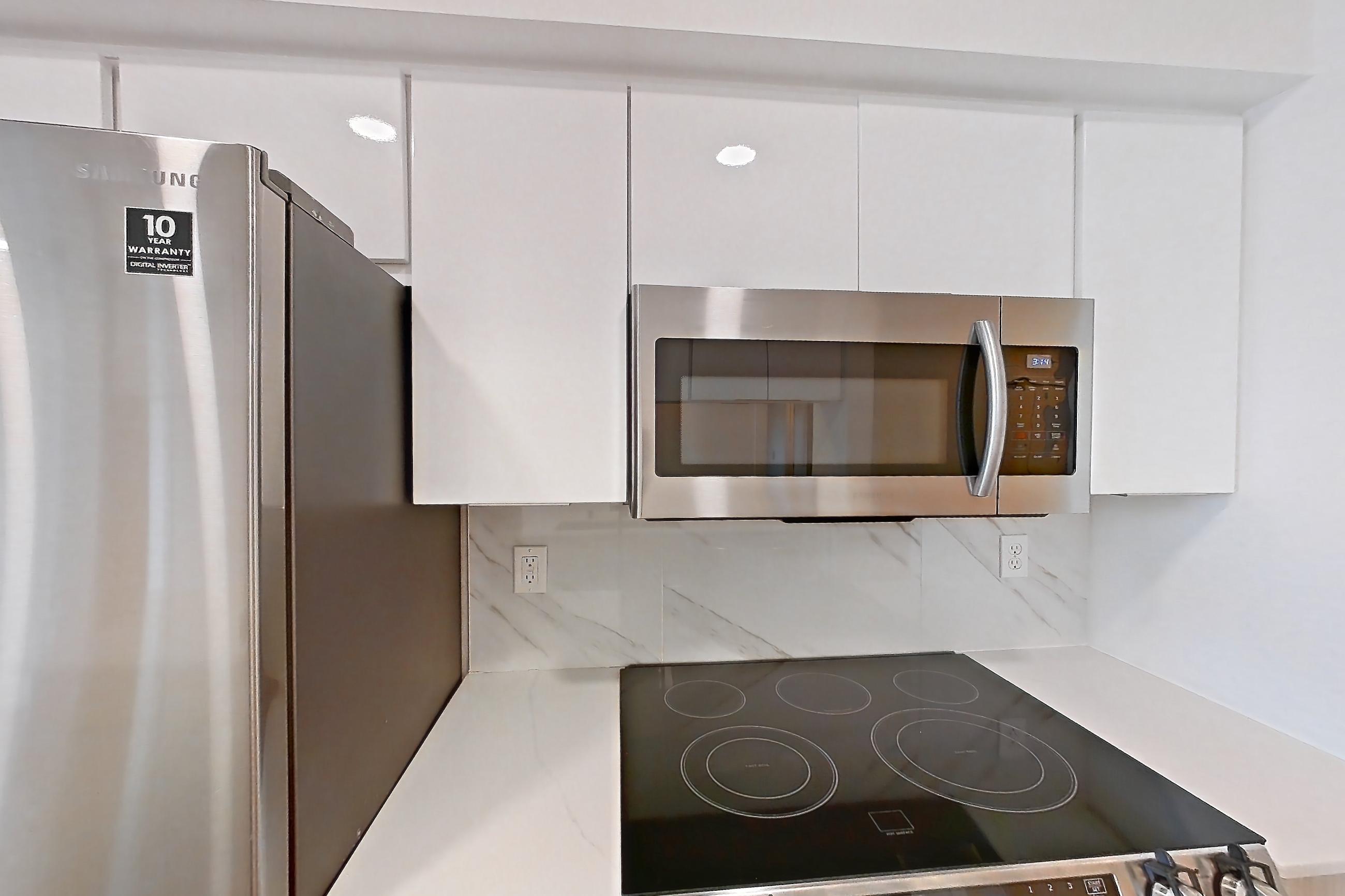 Kitchen with dishwasher, electric range, light countertops, light stone countertops, light wood-finish flooring, oven/range, refrigerator, and stainless steel appliances, Apartment 0004 at Eastlake 2851