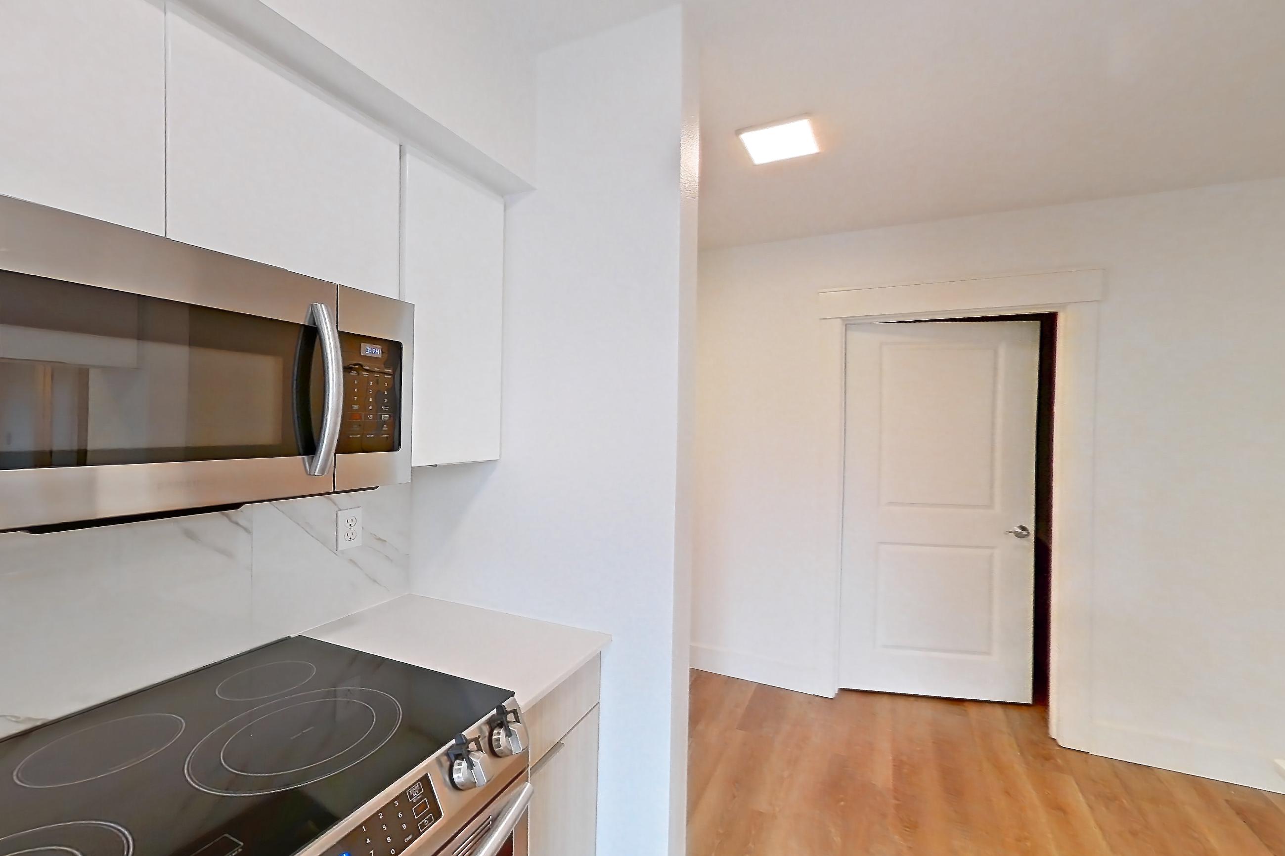 Kitchen with dishwasher, electric range, light countertops, light stone countertops, light wood-finish flooring, oven/range, refrigerator, and stainless steel appliances, Apartment 0004 at Eastlake 2851