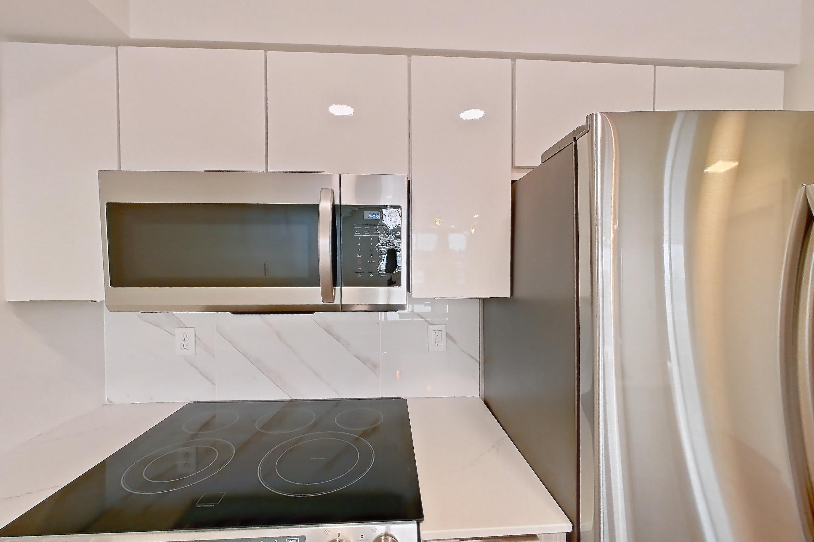 Kitchen with dishwasher, electric range, light countertops, light stone countertops, light wood-finish flooring, microwave, oven/range, refrigerator, and stainless steel appliances, Apartment 0328 at Eastlake 2851