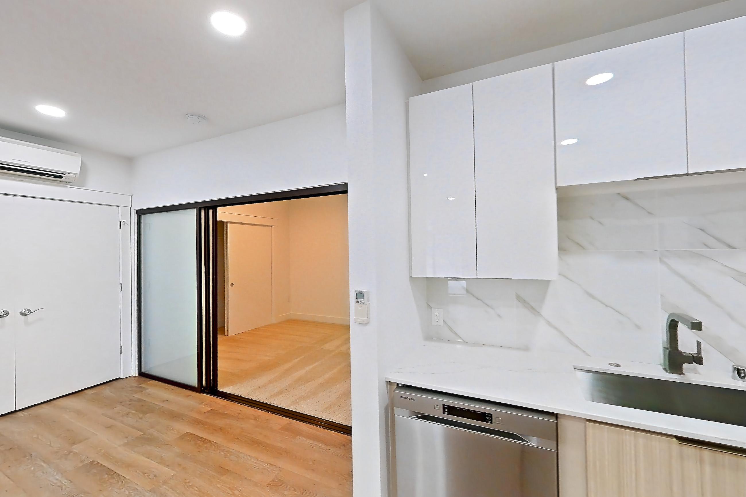 Kitchen with dishwasher, electric range, light countertops, light stone countertops, light wood-finish flooring, microwave, oven/range, refrigerator, and stainless steel appliances, Apartment 2835B at Eastlake 2851