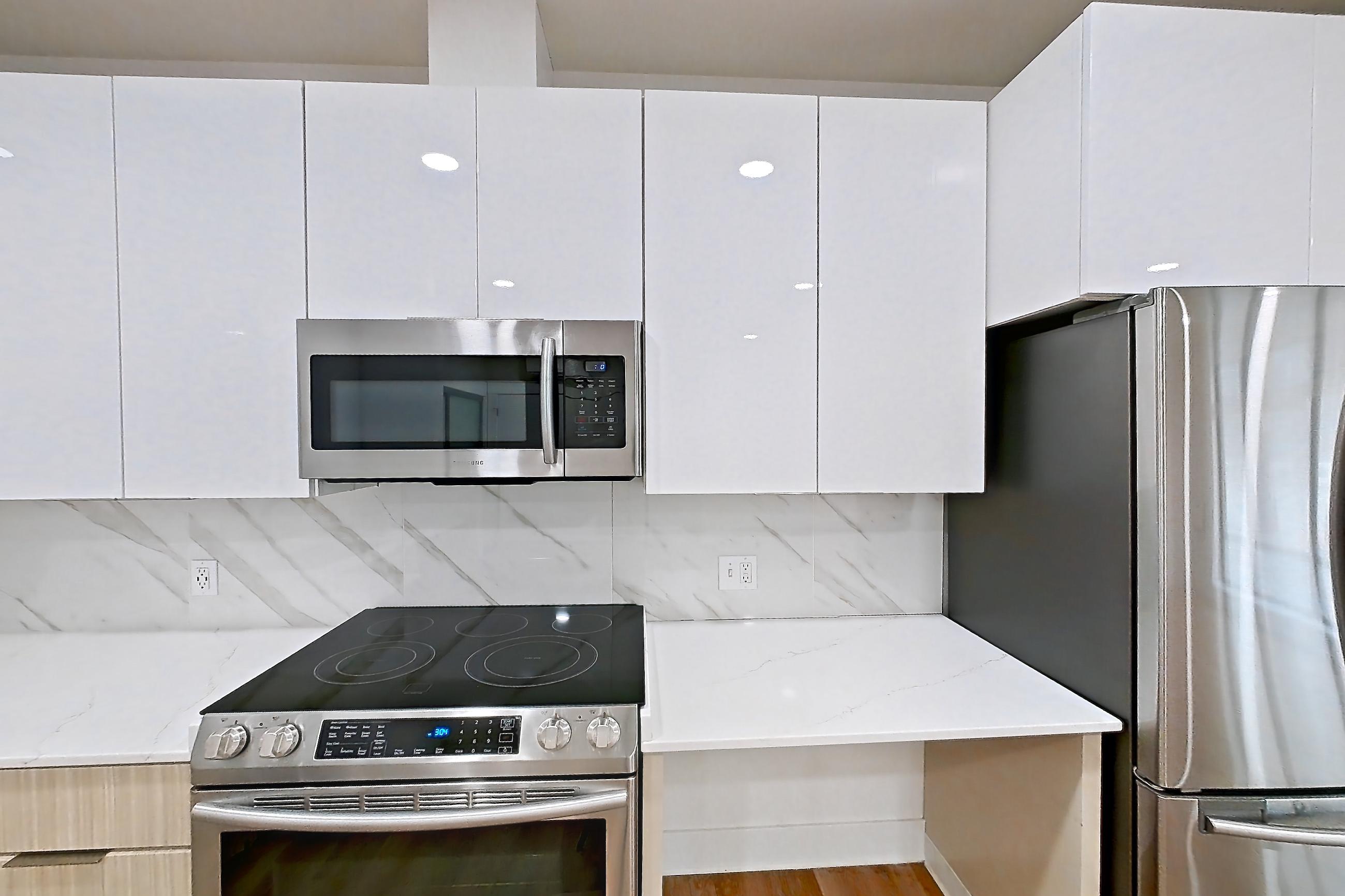 Kitchen with dishwasher, electric range, light countertops, light stone countertops, light wood-finish flooring, microwave, oven/range, refrigerator, and stainless steel appliances, Apartment 2835B at Eastlake 2851