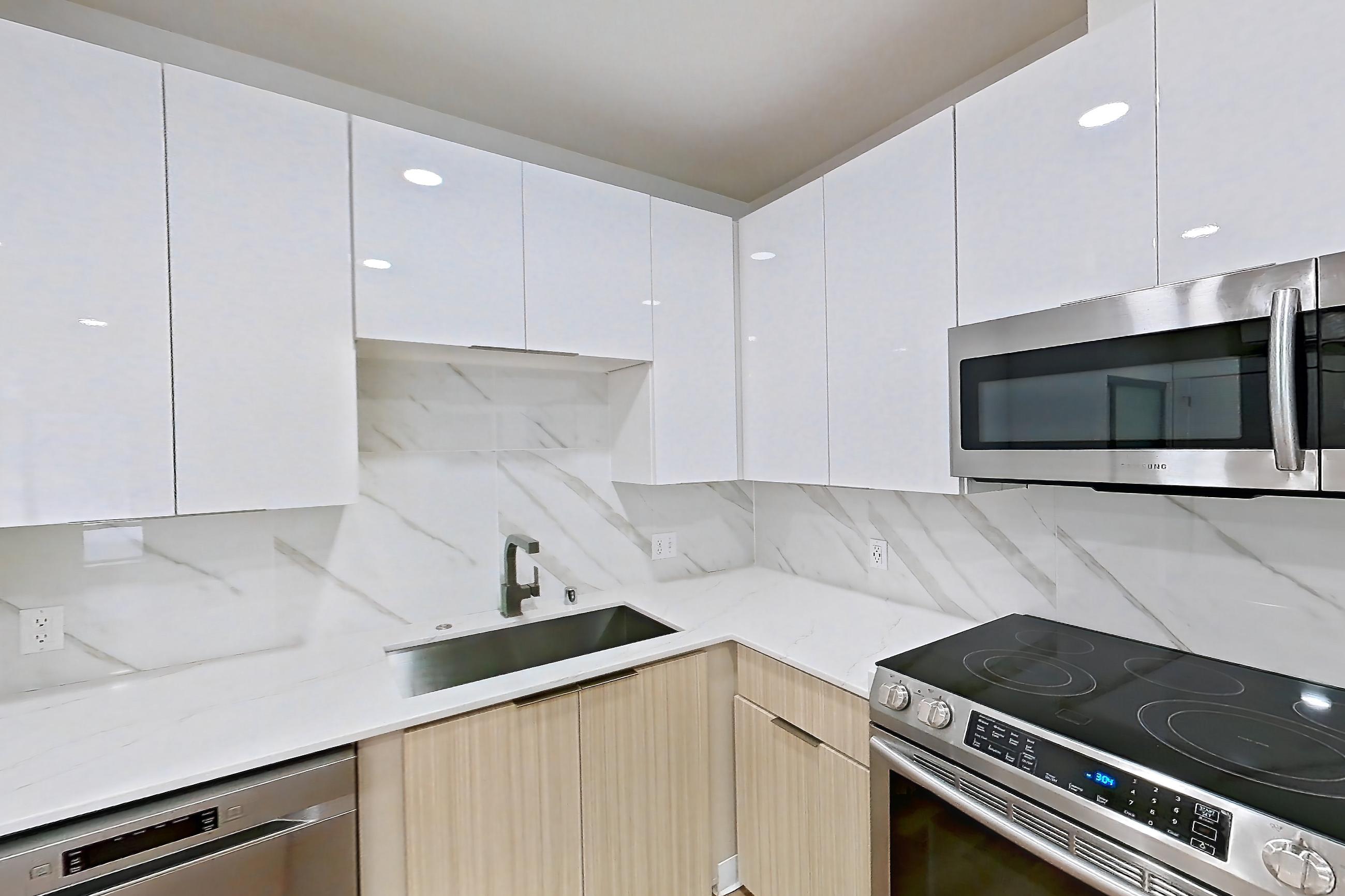 Kitchen with dishwasher, electric range, light countertops, light stone countertops, light wood-finish flooring, microwave, oven/range, refrigerator, and stainless steel appliances, Apartment 2835B at Eastlake 2851