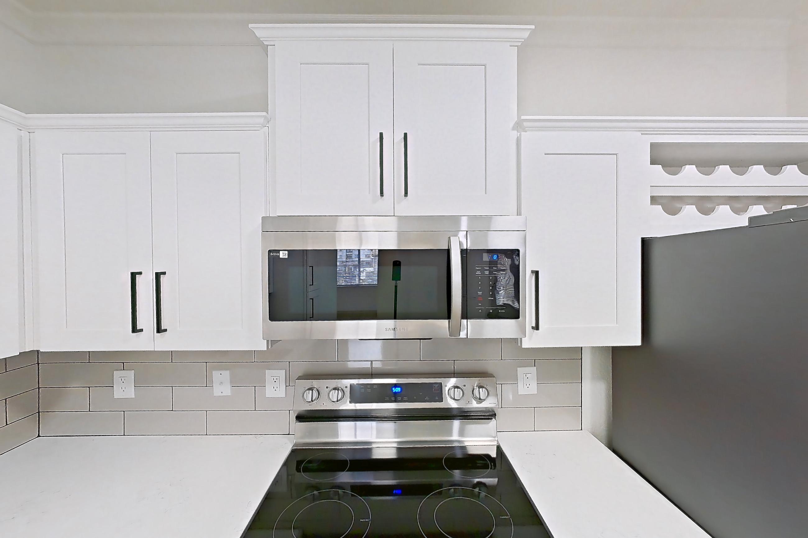 Kitchen with dishwasher, electric range, light countertops, light stone countertops, light wood-finish flooring, microwave, oven/range, refrigerator, and stainless steel appliances, Apartment 30-210 at Terracina