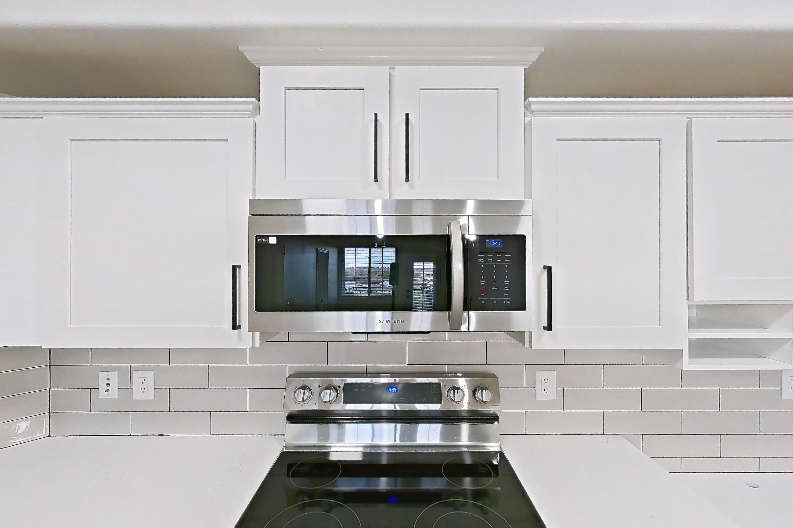 Kitchen with dishwasher, electric range, light countertops, light stone countertops, light wood-finish flooring, microwave, oven/range, refrigerator, and stainless steel appliances, Apartment 50-111 at Terracina