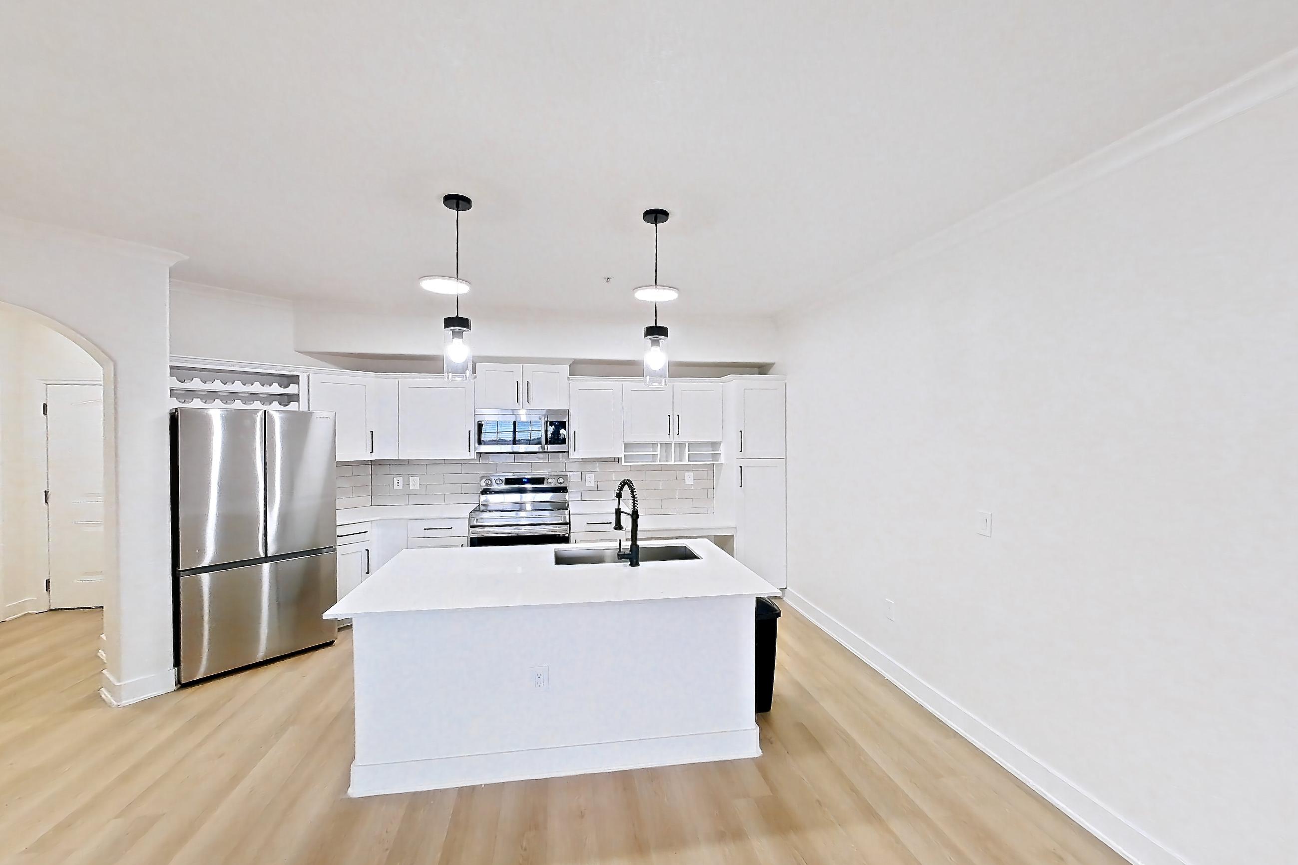 Living space with electric range, kitchen island, light countertops, light stone countertops, light wood-finish flooring, oven/range, refrigerator, and stainless steel appliances, Apartment 50-111 at Terracina