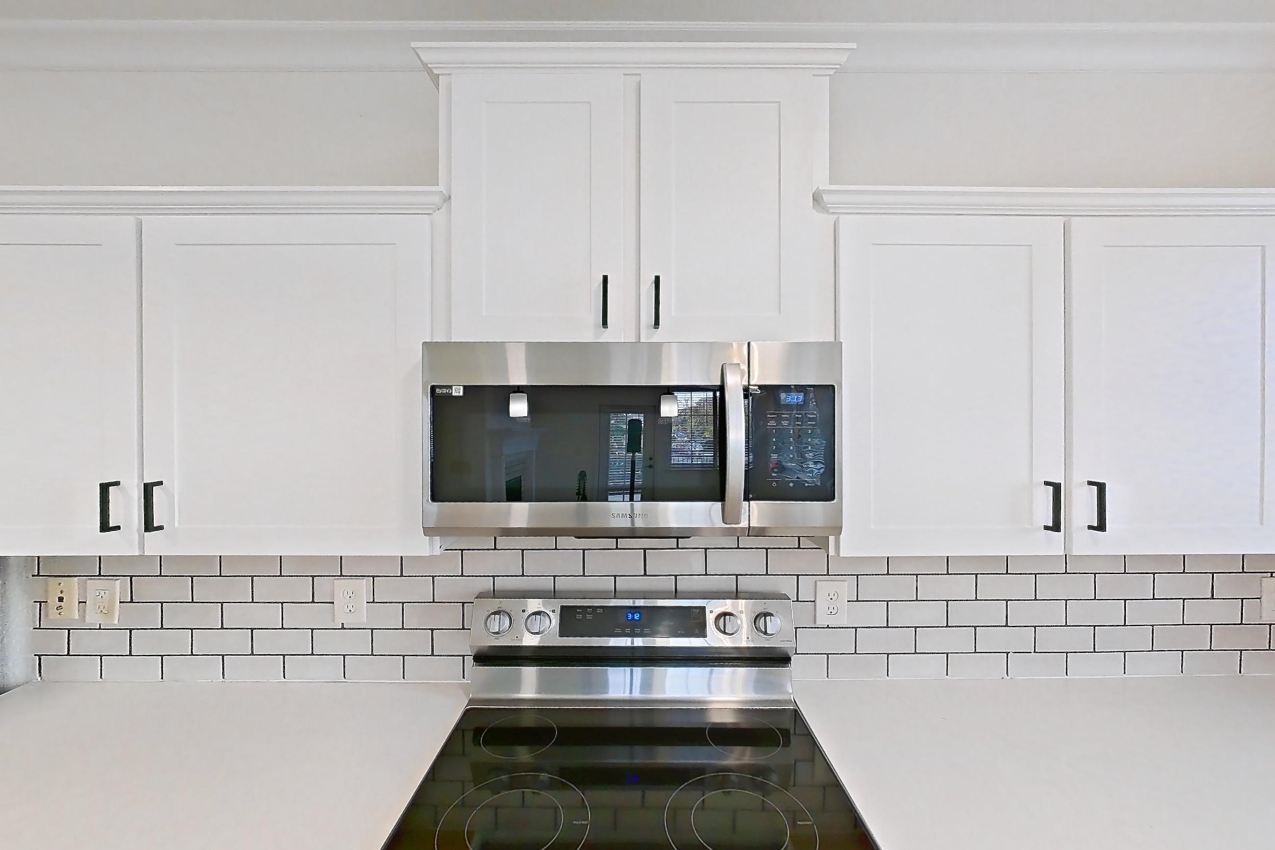 Kitchen with dishwasher, electric range, light countertops, light stone countertops, light wood-finish flooring, microwave, oven/range, refrigerator, and stainless steel appliances, Apartment 60-207 at Terracina