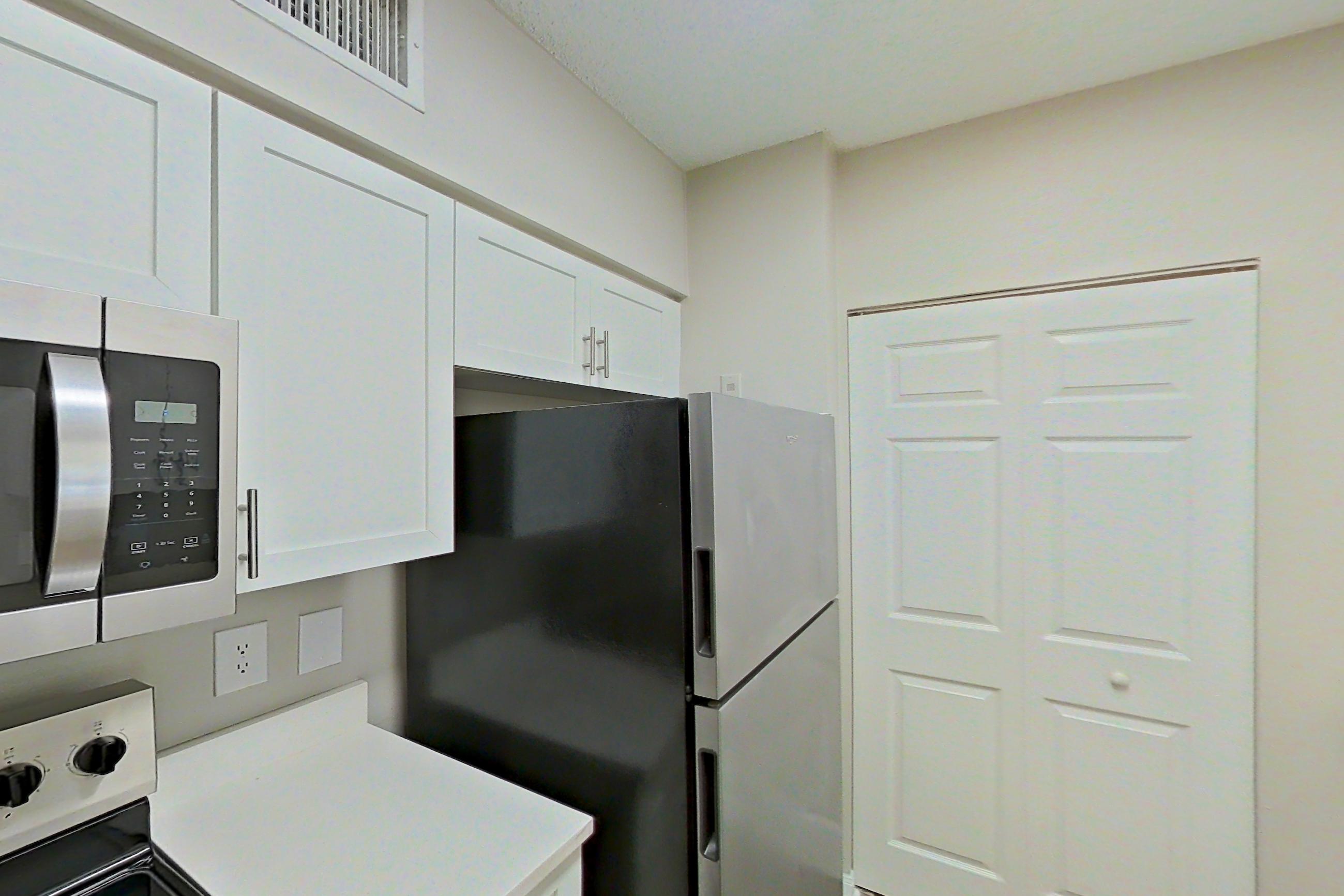 Kitchen with dishwasher, electric range, light countertops, light stone countertops, light wood-finish flooring, refrigerator, and stainless steel appliances, Apartment 15-207 at Miramar Lakes