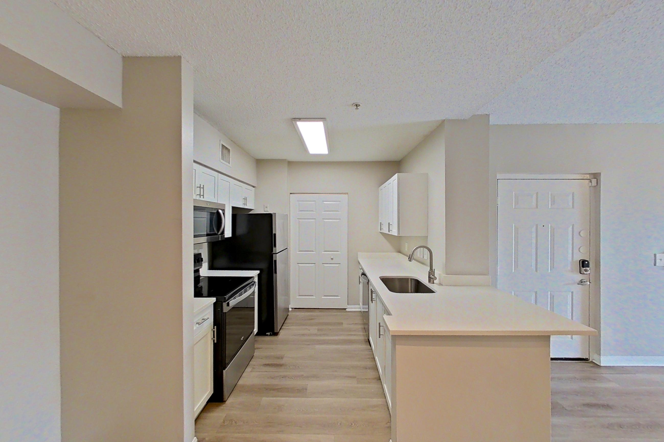 Living space with dishwasher, electric range, light stone countertops, light wood-finish flooring, oven/range, and stainless steel appliances, Apartment 15-207 at Miramar Lakes