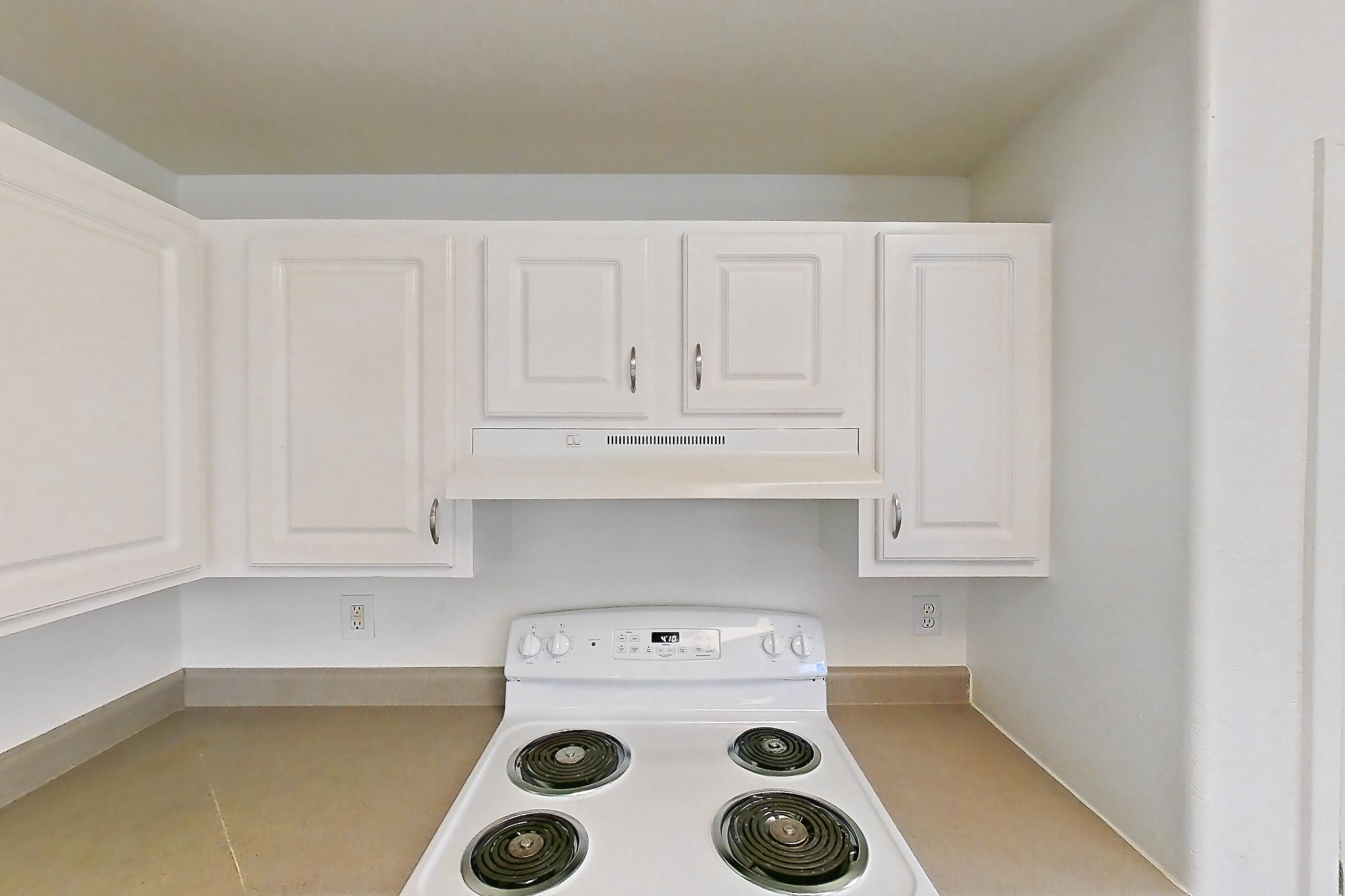 Kitchen with electric range, fireplace, light countertops, light wood-finish flooring, oven/range, range hood, tile fireplace, and white appliances, Apartment 12-105 at Eagle Ridge