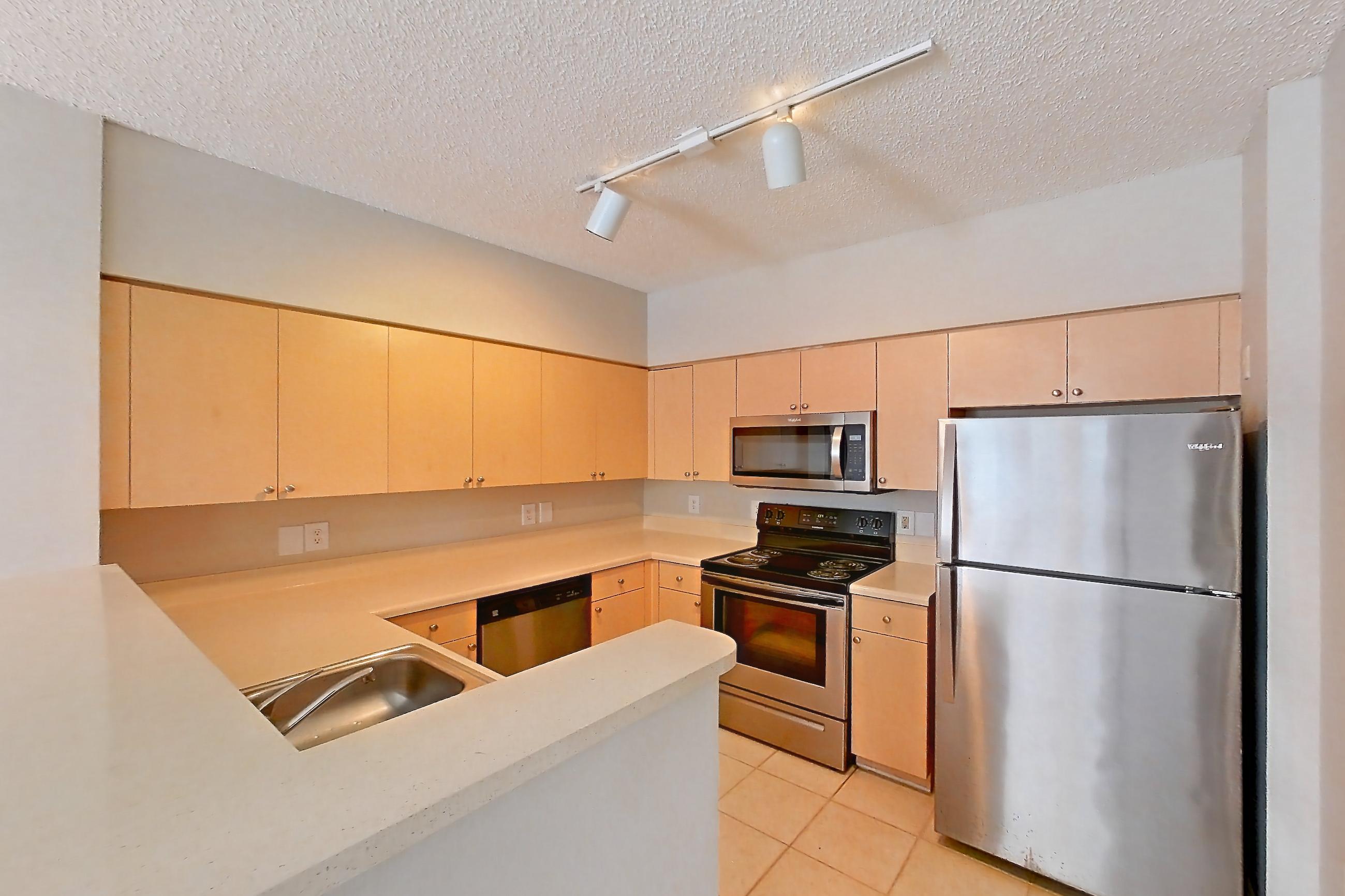 Kitchen entryway with dishwasher, electric range, light countertops, light tile flooring, light wood-finish flooring, microwave, oven/range, refrigerator, and stainless steel appliances, Apartment 06-108 at Miramar Lakes