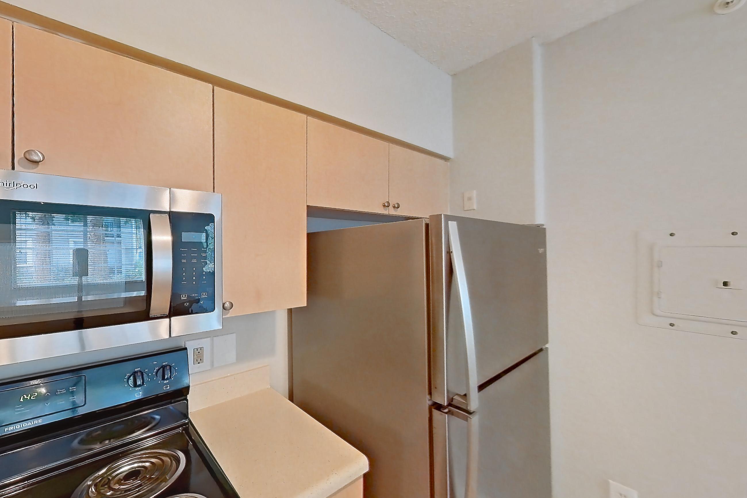 Kitchen with dishwasher, electric range, light countertops, light tile flooring, microwave, refrigerator, and stainless steel appliances, Apartment 06-108 at Miramar Lakes