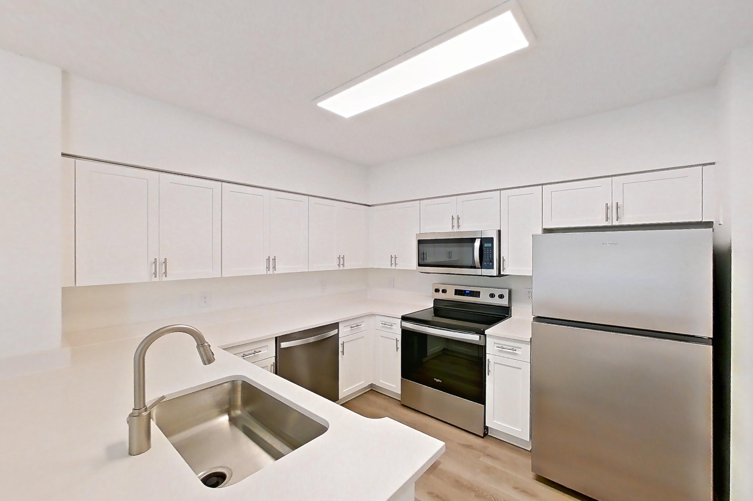 Kitchen entryway with dishwasher, electric range, light countertops, light wood-finish flooring, microwave, oven/range, refrigerator, and stainless steel appliances, Apartment 15-208 at Miramar Lakes