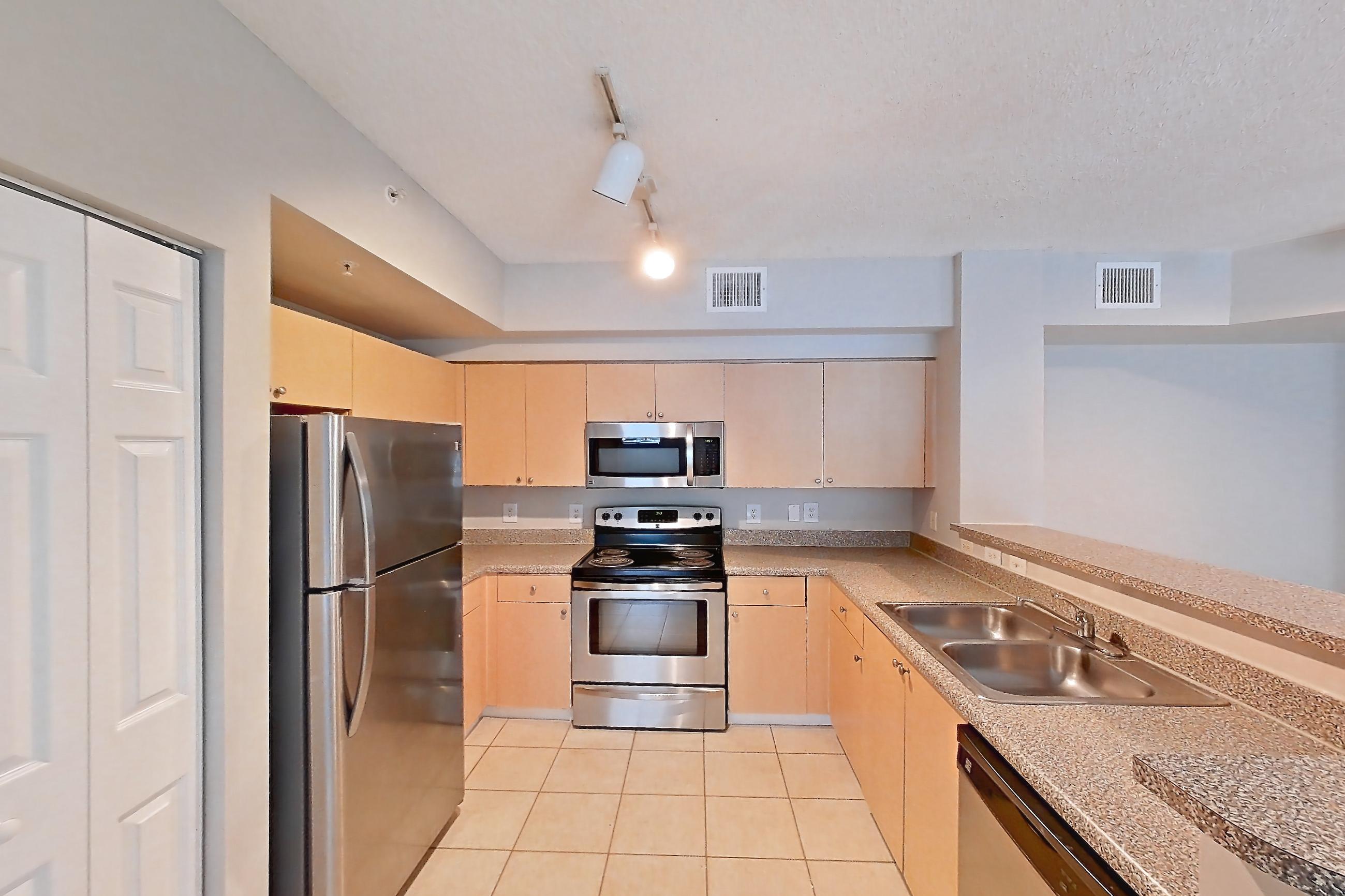 Kitchen entryway with cooktop, dark tile flooring, dark wood-finish flooring, dishwasher, electric range, light countertops, light tile flooring, oven/range, refrigerator, and stainless steel appliances, Apartment 10-105 at Miramar Lakes