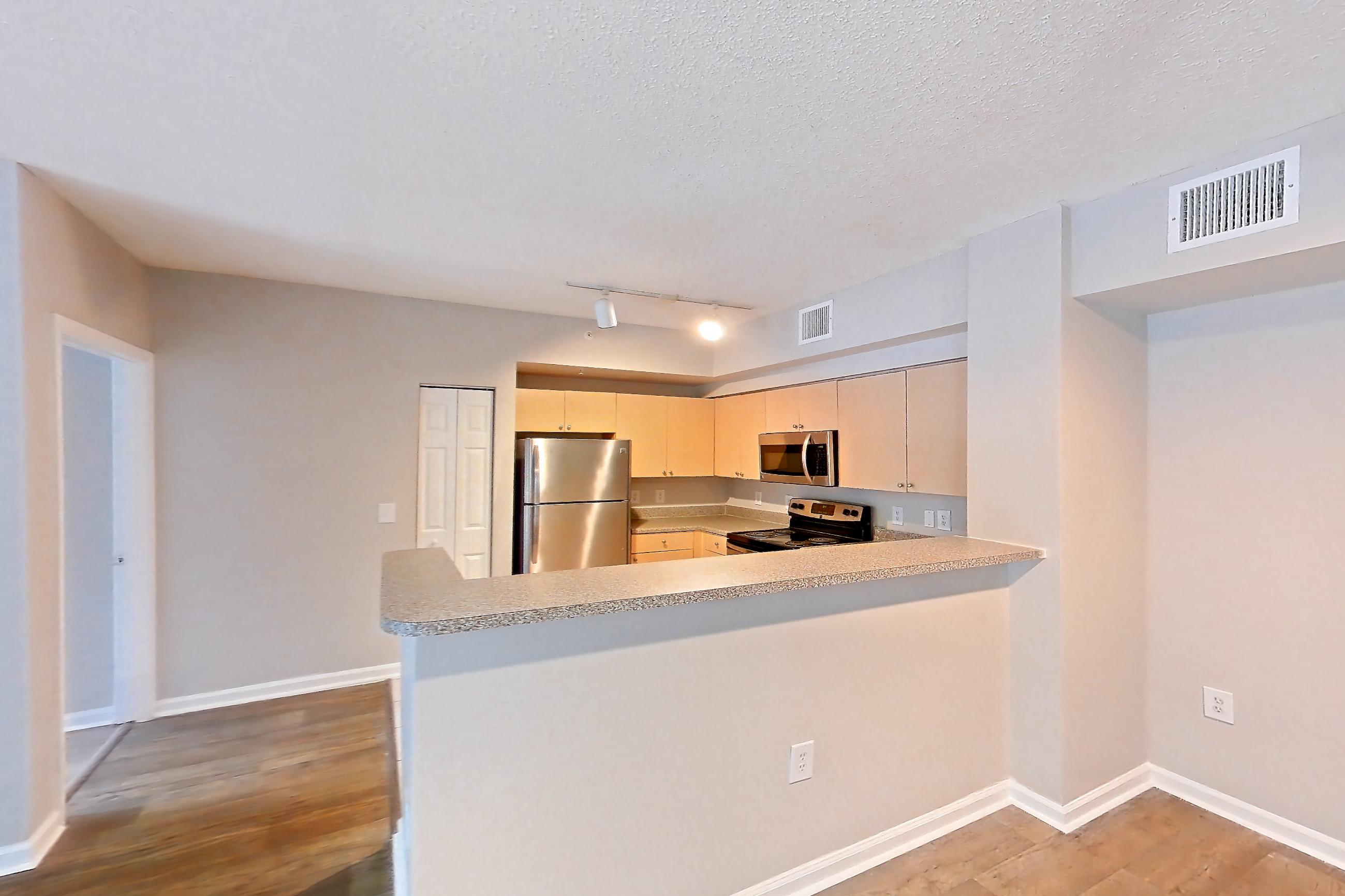Living space with dark wood-finish flooring, electric range, light countertops, light wood-finish flooring, microwave, oven/range, refrigerator, and stainless steel appliances, Apartment 10-105 at Miramar Lakes