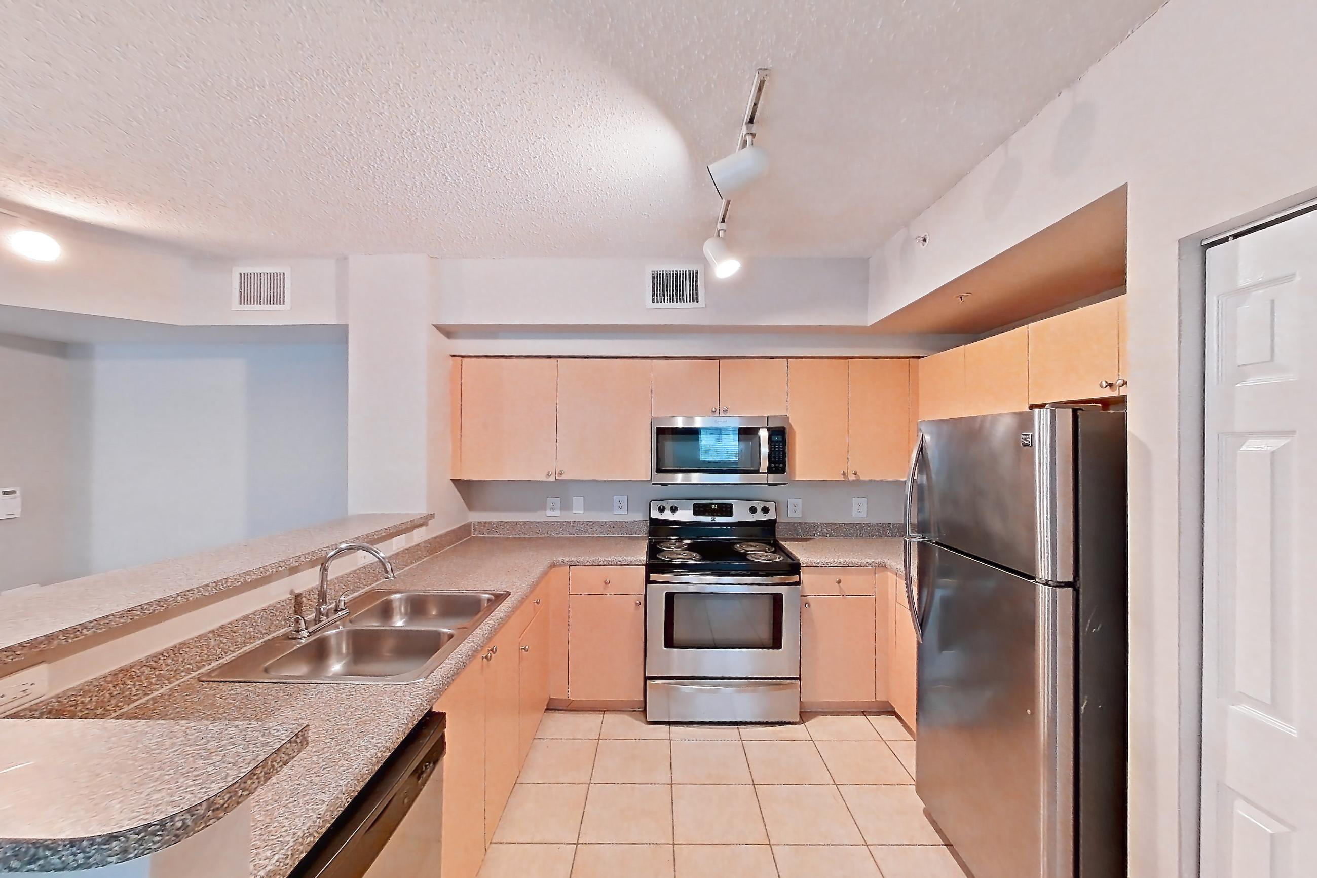 Kitchen entryway with dishwasher, electric range, light countertops, light tile flooring, light wood-finish flooring, microwave, oven/range, refrigerator, and stainless steel appliances, Apartment 10-106 at Miramar Lakes