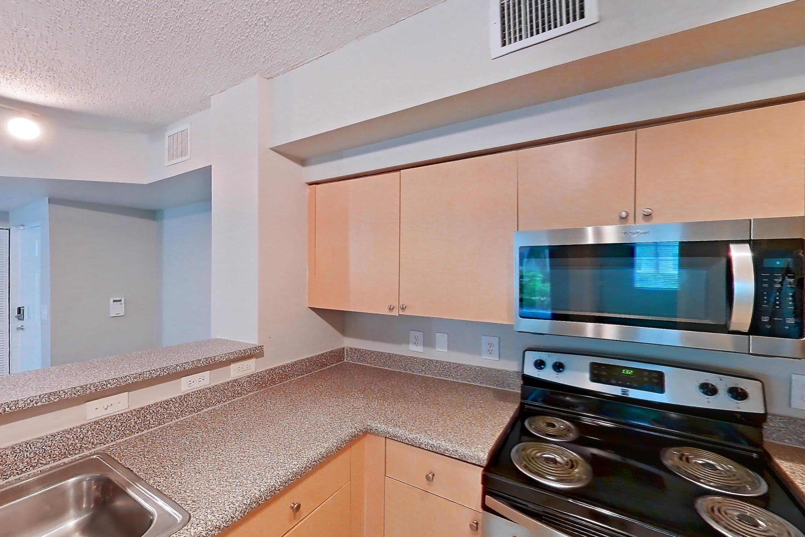 Kitchen with dishwasher, electric range, light countertops, light tile flooring, microwave, oven/range, and stainless steel appliances, Apartment 10-106 at Miramar Lakes