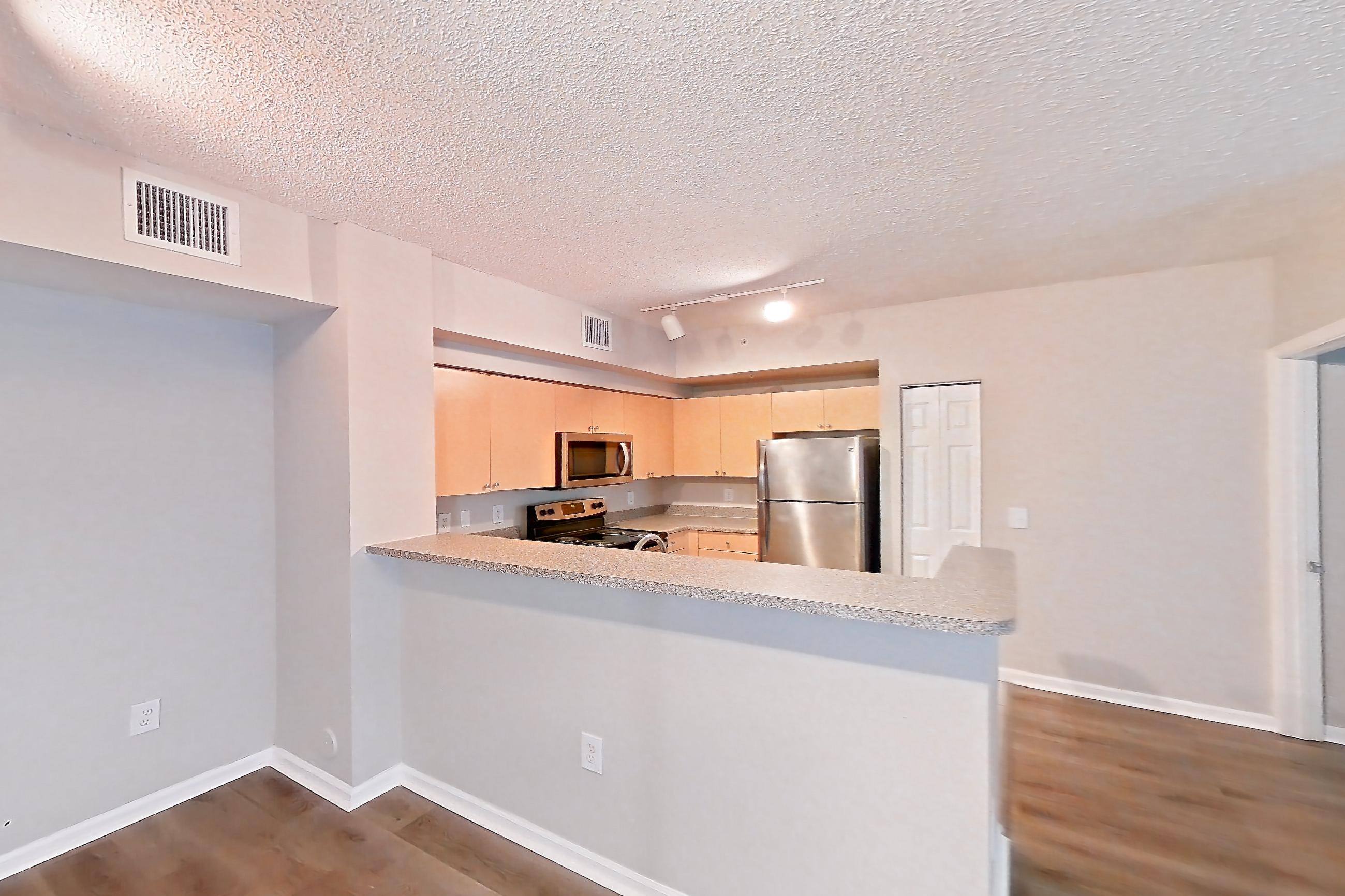 Living space with dark wood-finish flooring, electric range, light countertops, light wood-finish flooring, microwave, oven/range, refrigerator, and stainless steel appliances, Apartment 10-106 at Miramar Lakes