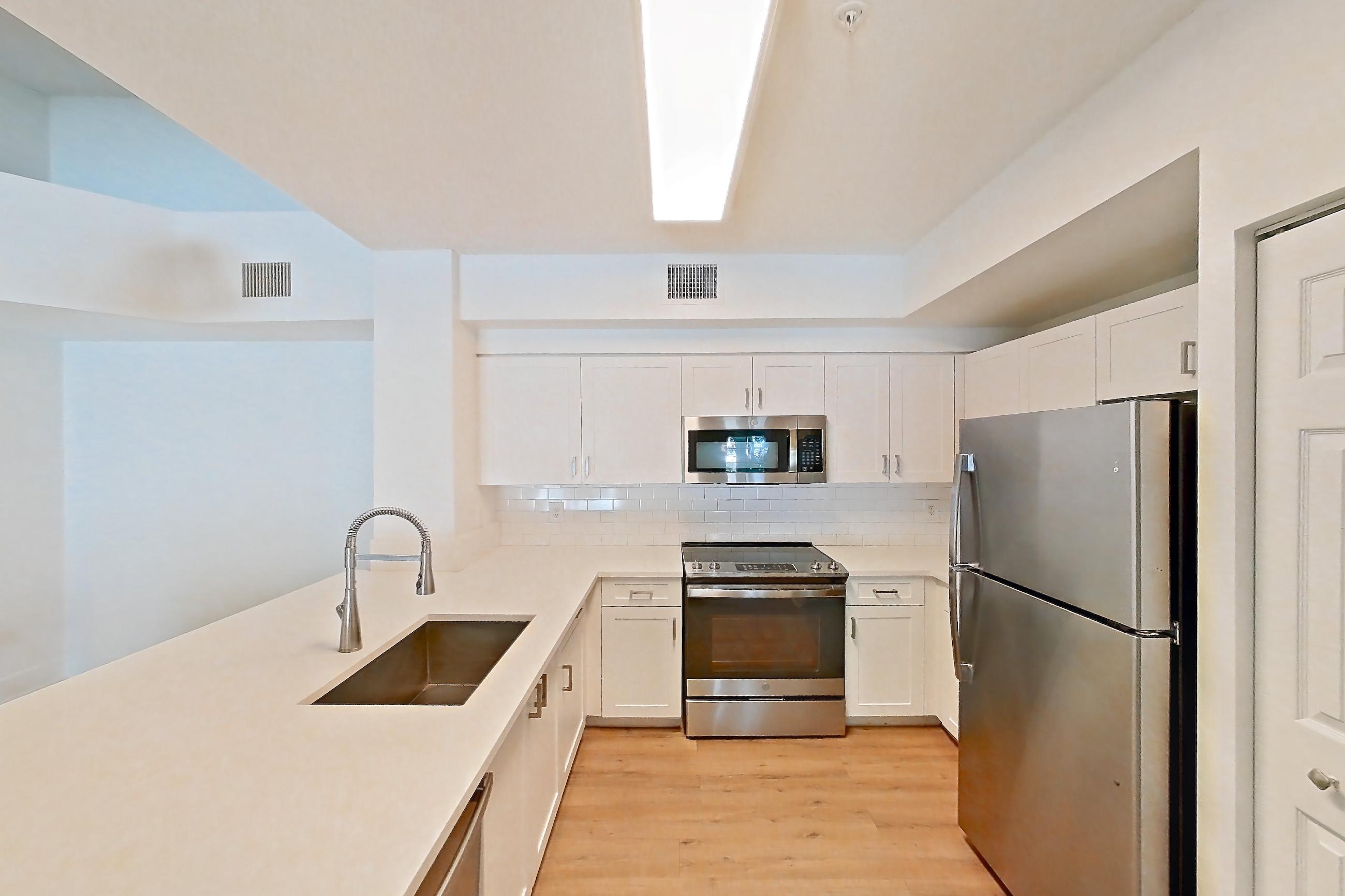 Kitchen entryway with dishwasher, electric range, light countertops, light stone countertops, light wood-finish flooring, oven/range, refrigerator, and stainless steel appliances, Apartment 01-208 at Miramar Lakes