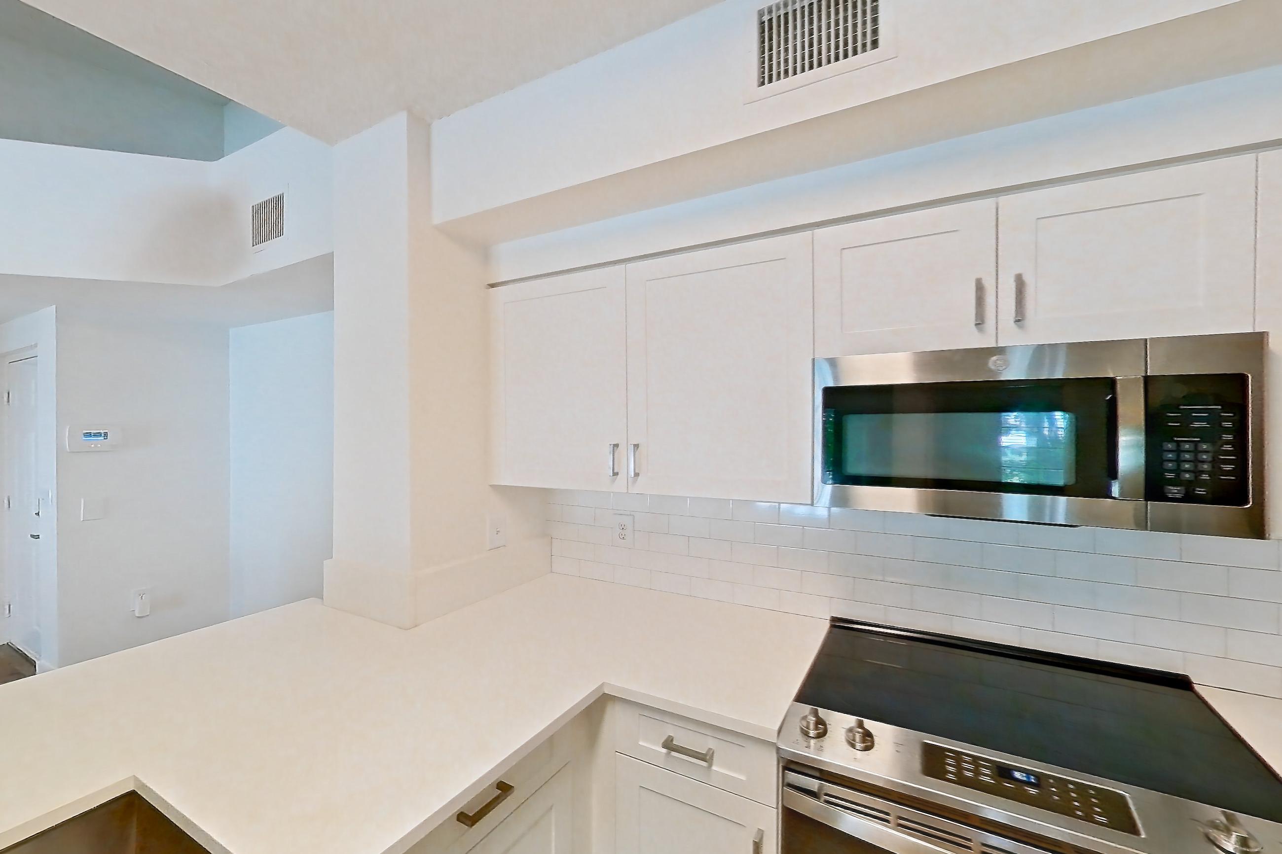 Kitchen with dishwasher, electric range, light countertops, light stone countertops, light wood-finish flooring, microwave, oven/range, and stainless steel appliances, Apartment 01-208 at Miramar Lakes