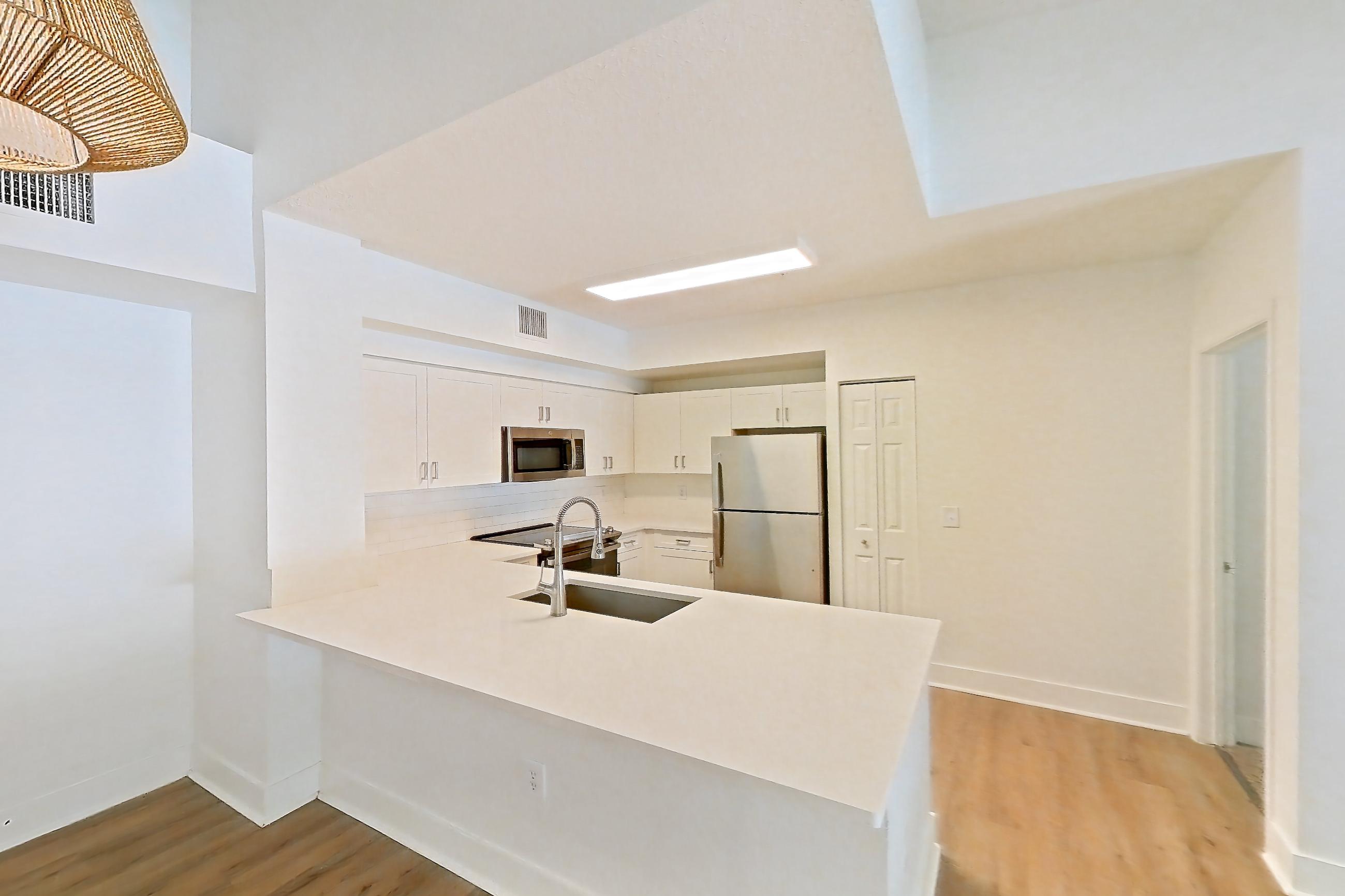 Living space with light stone countertops, light wood-finish flooring, refrigerator, and stainless steel appliances, Apartment 01-208 at Miramar Lakes