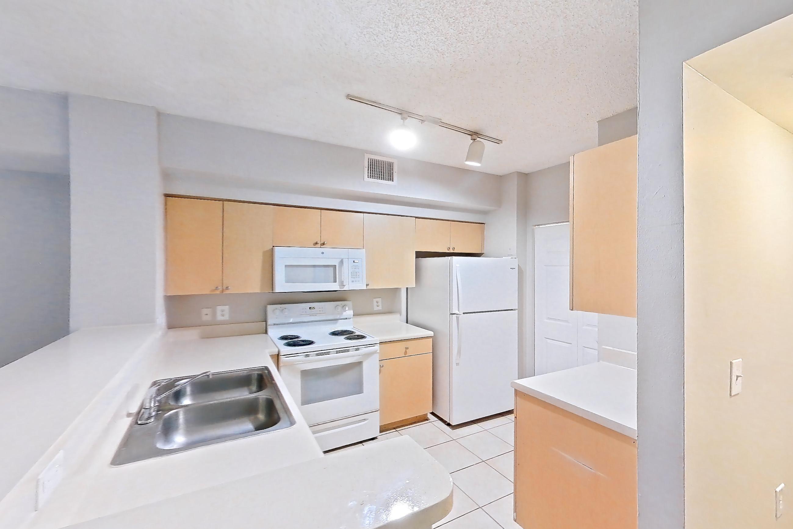 Kitchen entryway with electric range, light countertops, light tile flooring, light wood-finish flooring, microwave, oven/range, refrigerator, and white appliances, Apartment 12-207 at Miramar Lakes
