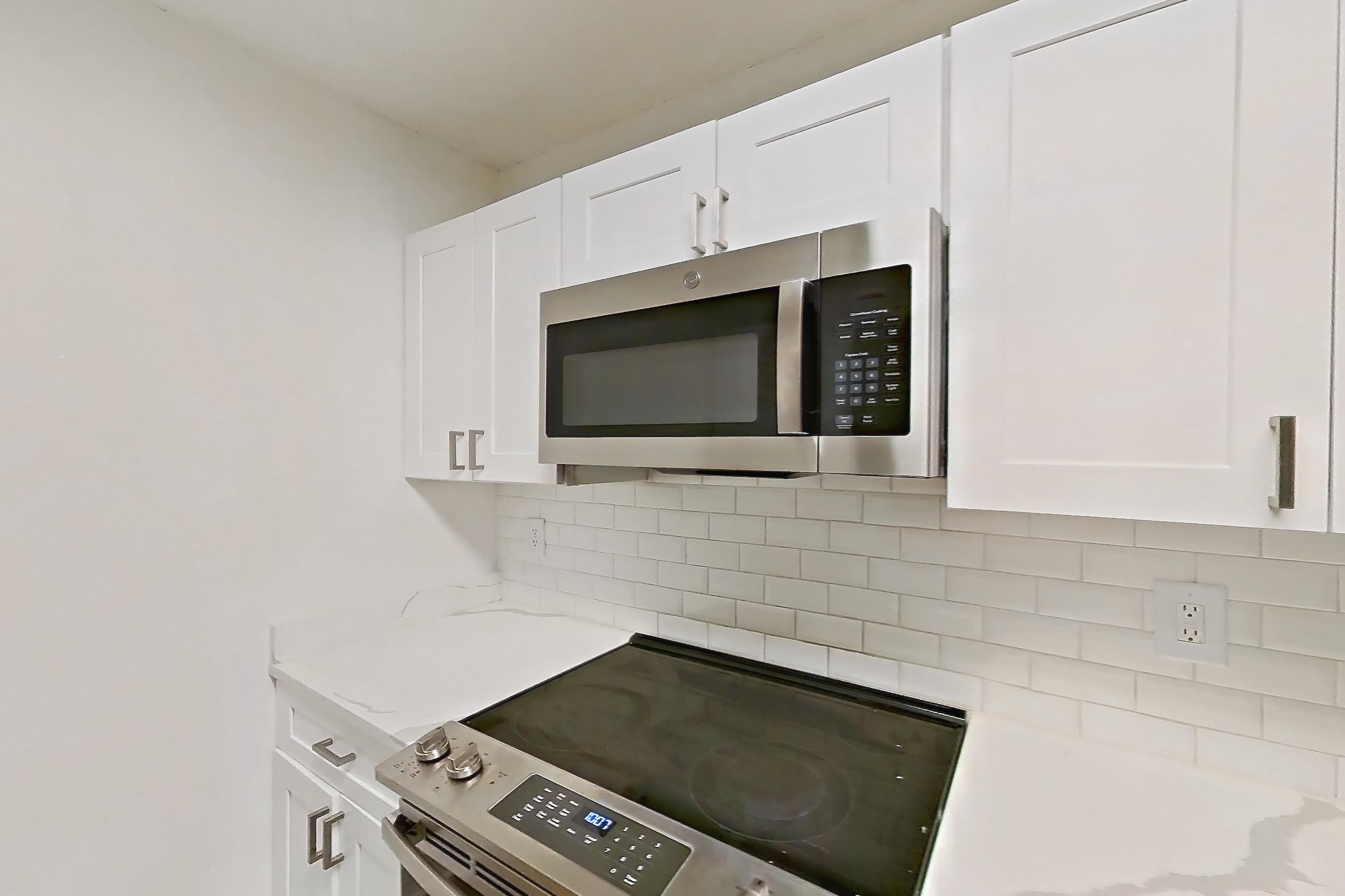 Kitchen with dishwasher, electric range, light countertops, light stone countertops, light wood-finish flooring, microwave, oven/range, and stainless steel appliances, Apartment 0211 at The Dawson