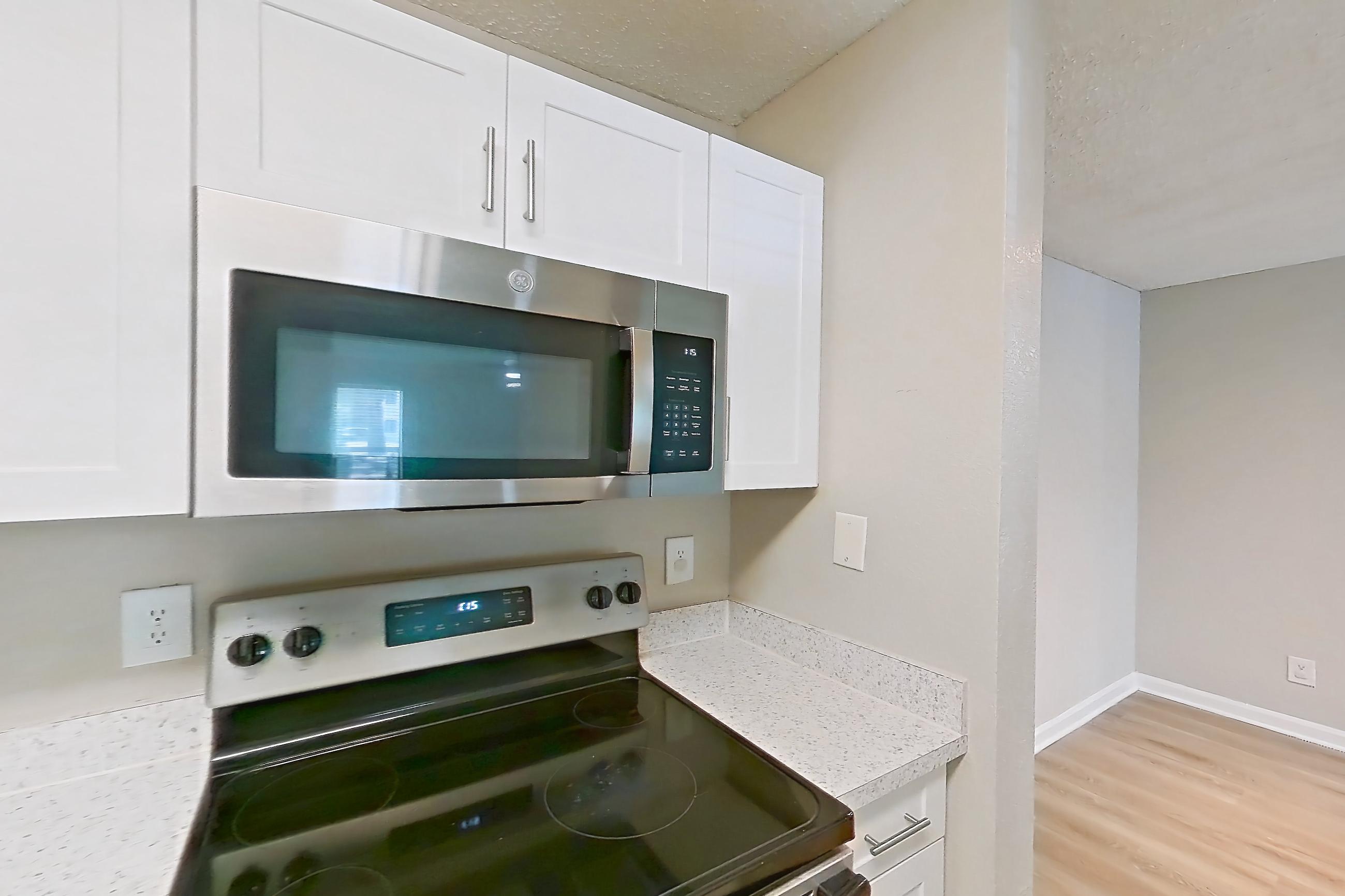 Kitchen with dishwasher, electric range, light countertops, light stone countertops, light wood-finish flooring, microwave, oven/range, refrigerator, and stainless steel appliances, Apartment 0403 at The Dawson