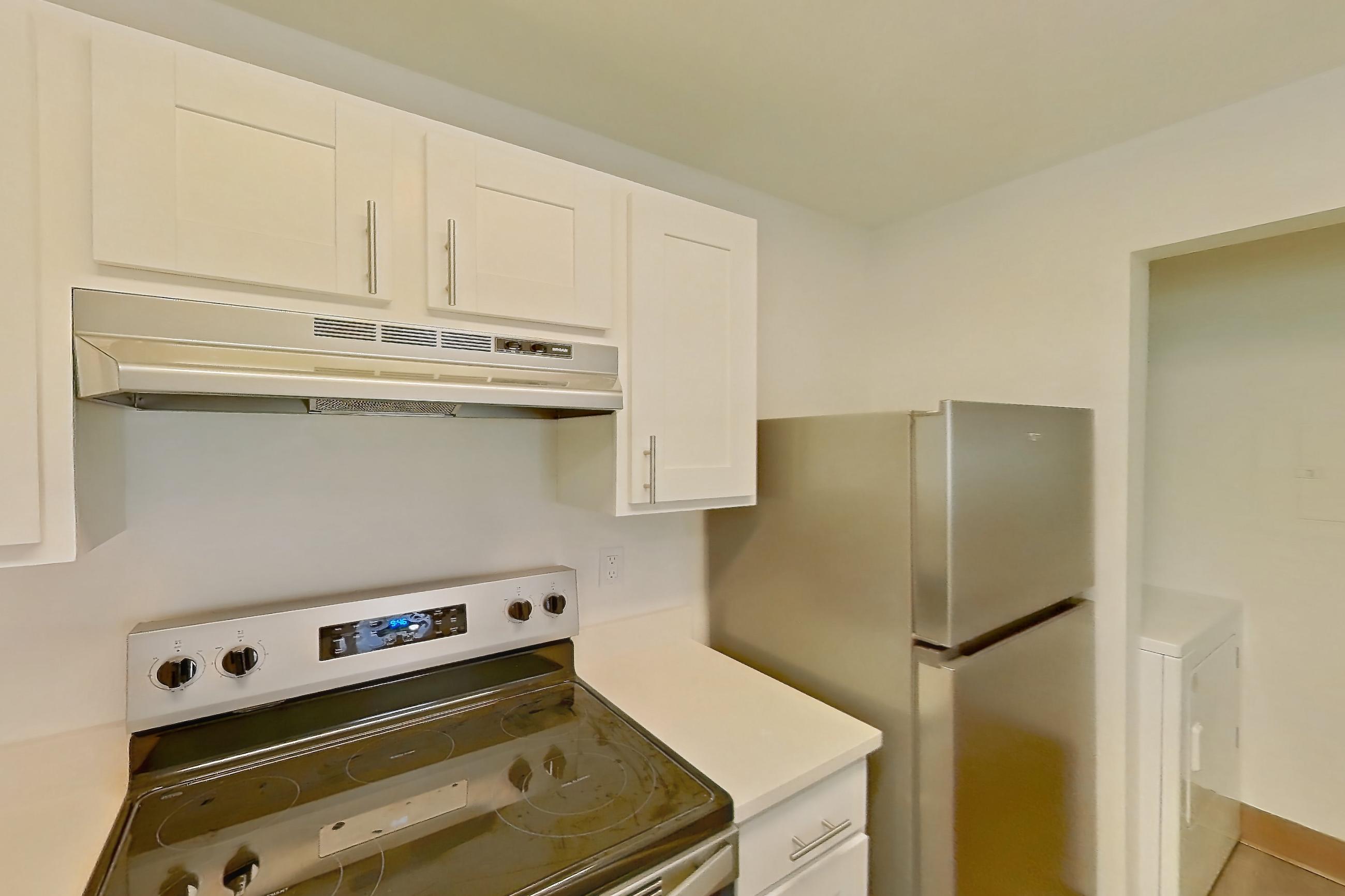 Kitchen with electric range, fireplace, light countertops, light wood-finish flooring, oven/range, refrigerator, and stainless steel appliances, Apartment 18K at Stillwater