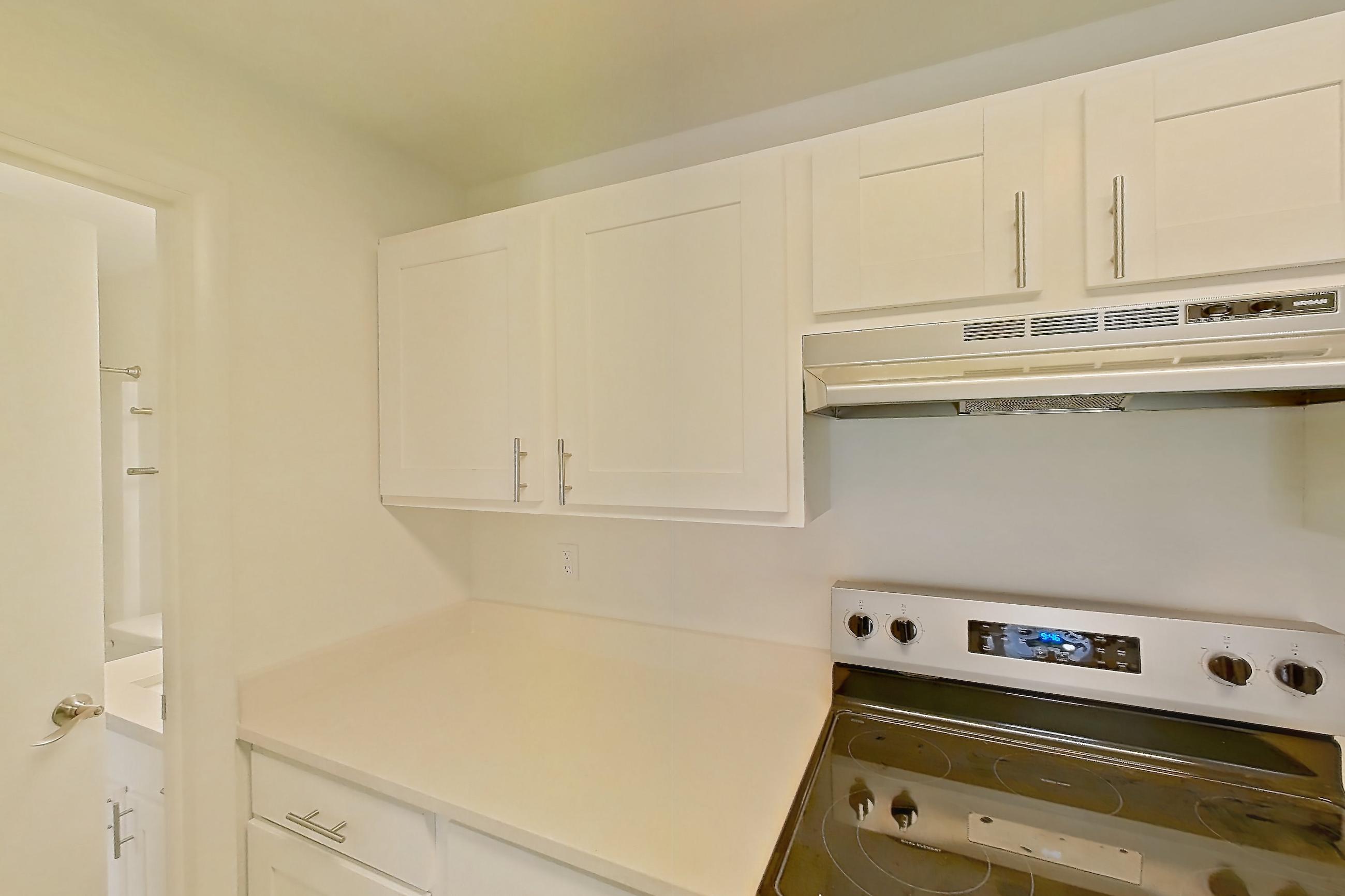 Kitchen with electric range, fireplace, light countertops, light wood-finish flooring, oven/range, refrigerator, and stainless steel appliances, Apartment 18K at Stillwater