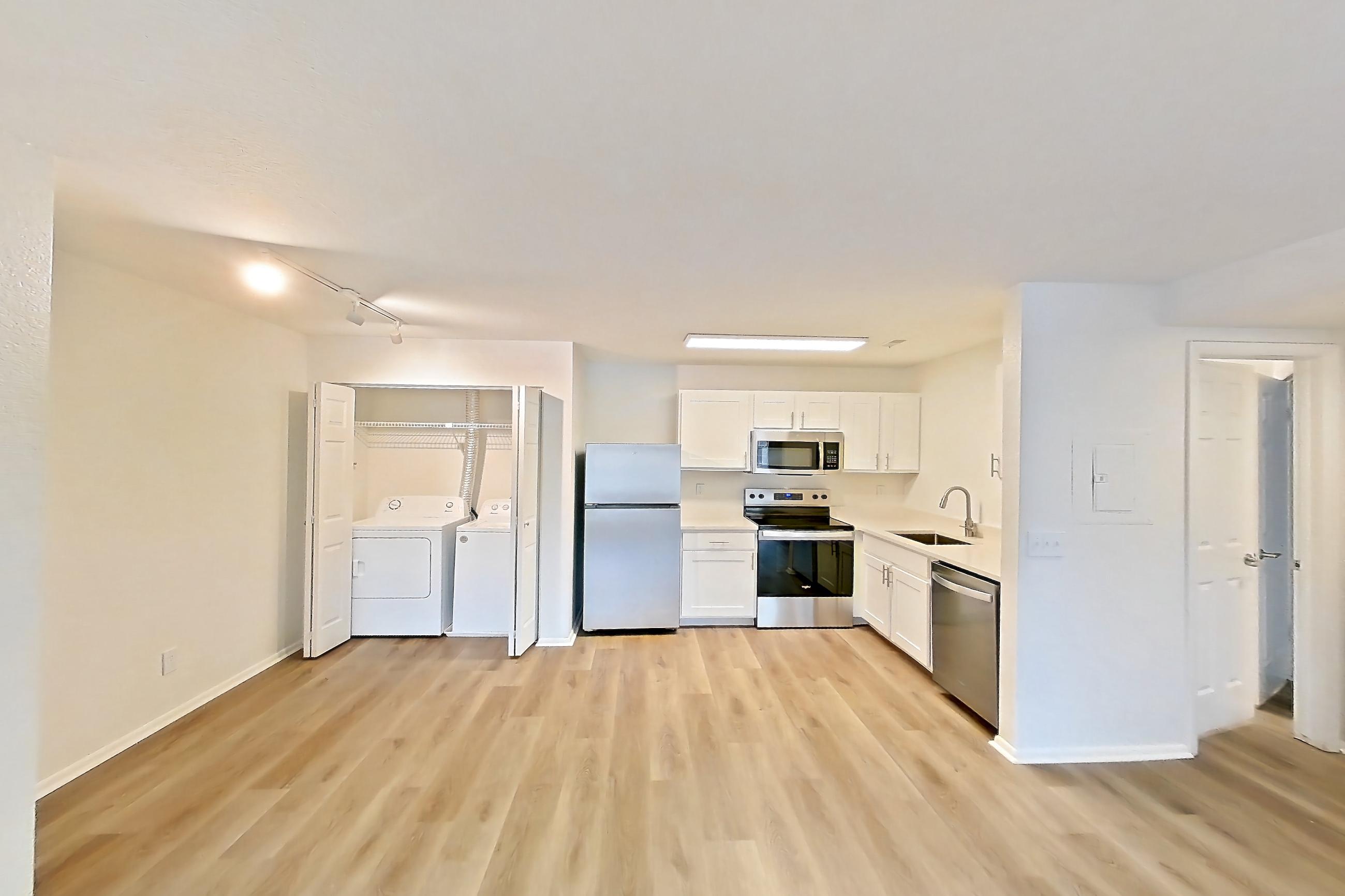 Living room with dishwasher, electric range, in-unit laundry, light countertops, light wood-finish flooring, oven/range, refrigerator, and stainless steel appliances, Apartment 06P at Stillwater