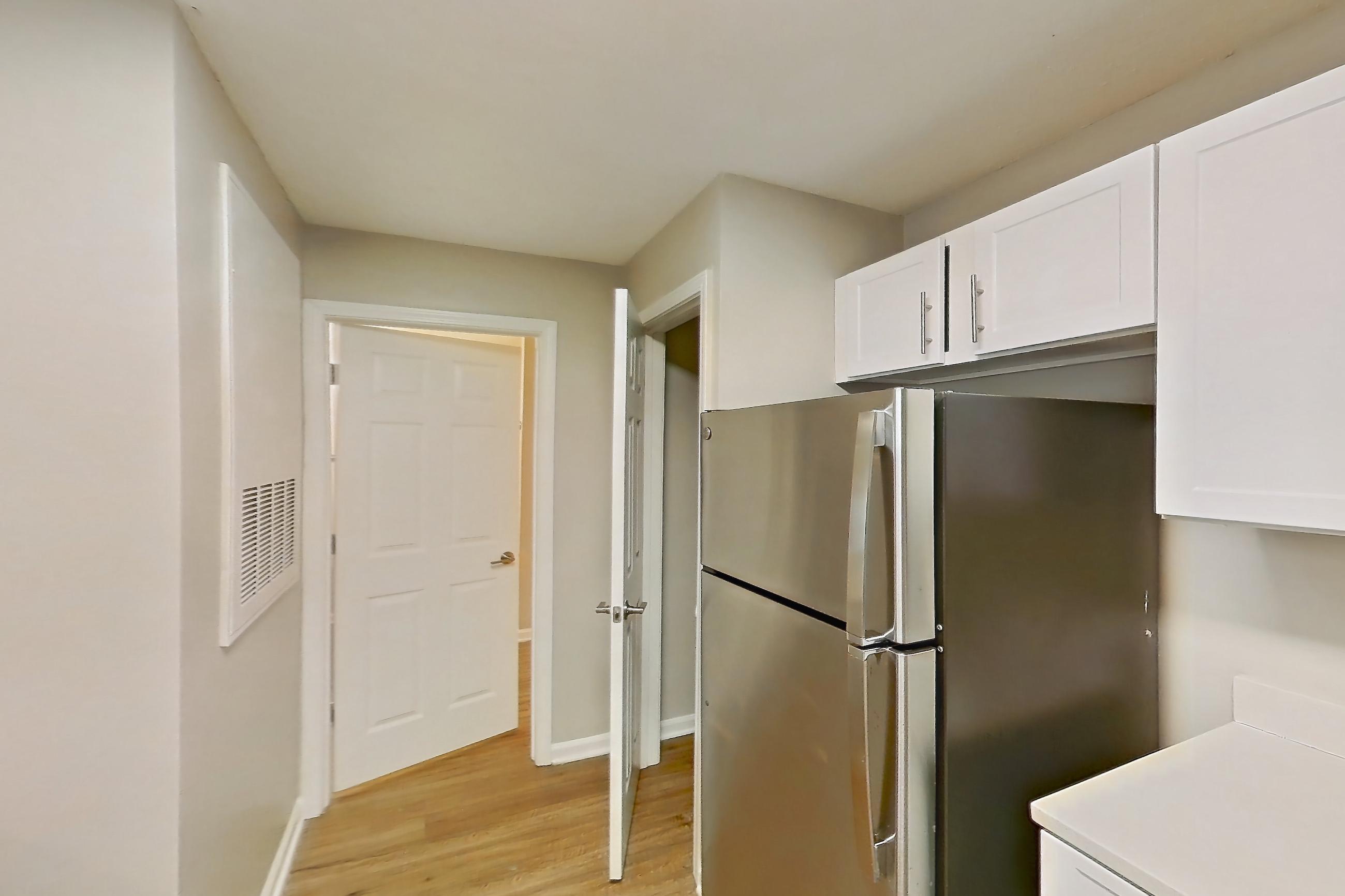 Kitchen with black appliances, dishwasher, electric range, light countertops, light wood-finish flooring, oven/range, range hood, refrigerator, and stainless steel appliances, Apartment 6425-3C at Ashford Place