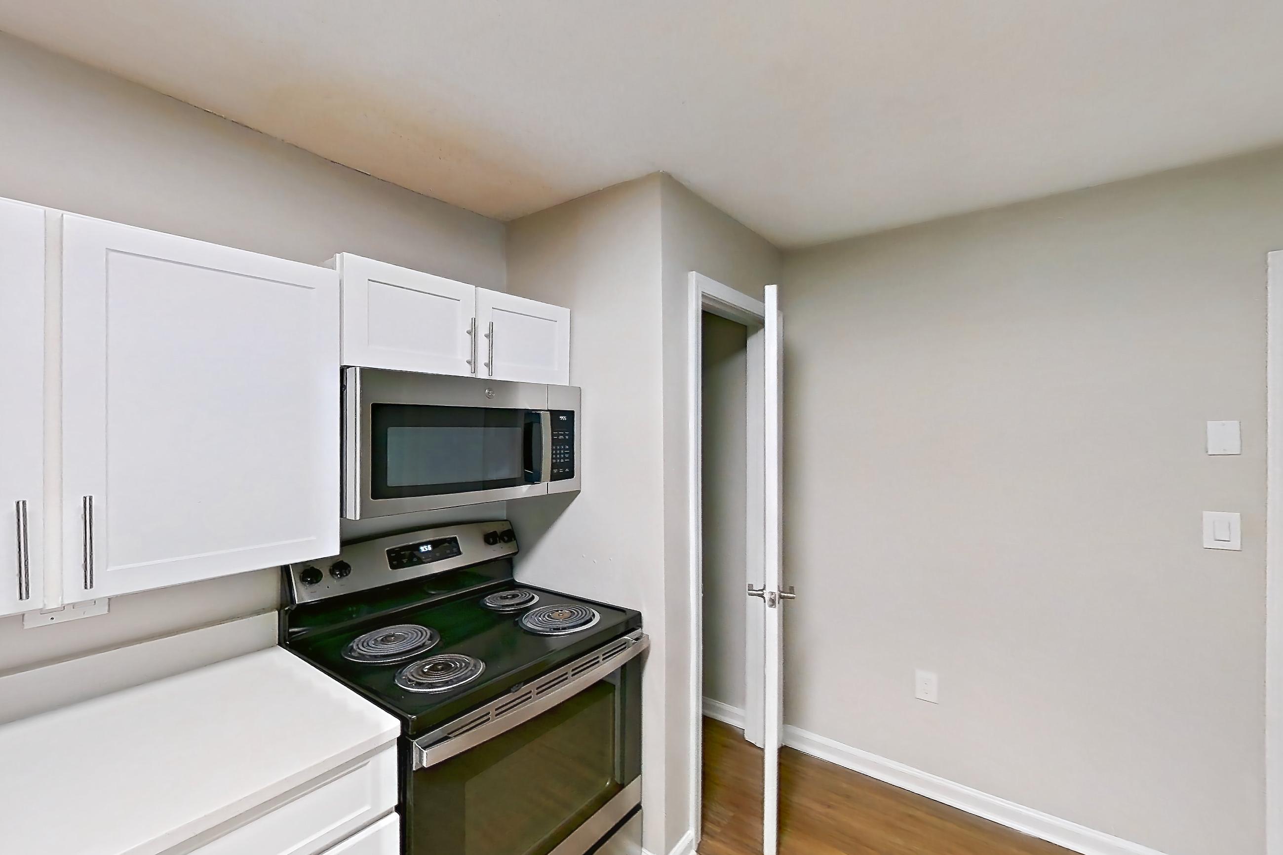 Kitchen with dishwasher, electric range, light countertops, light wood-finish flooring, microwave, oven/range, and stainless steel appliances, Apartment 6515-1C at Ashford Place