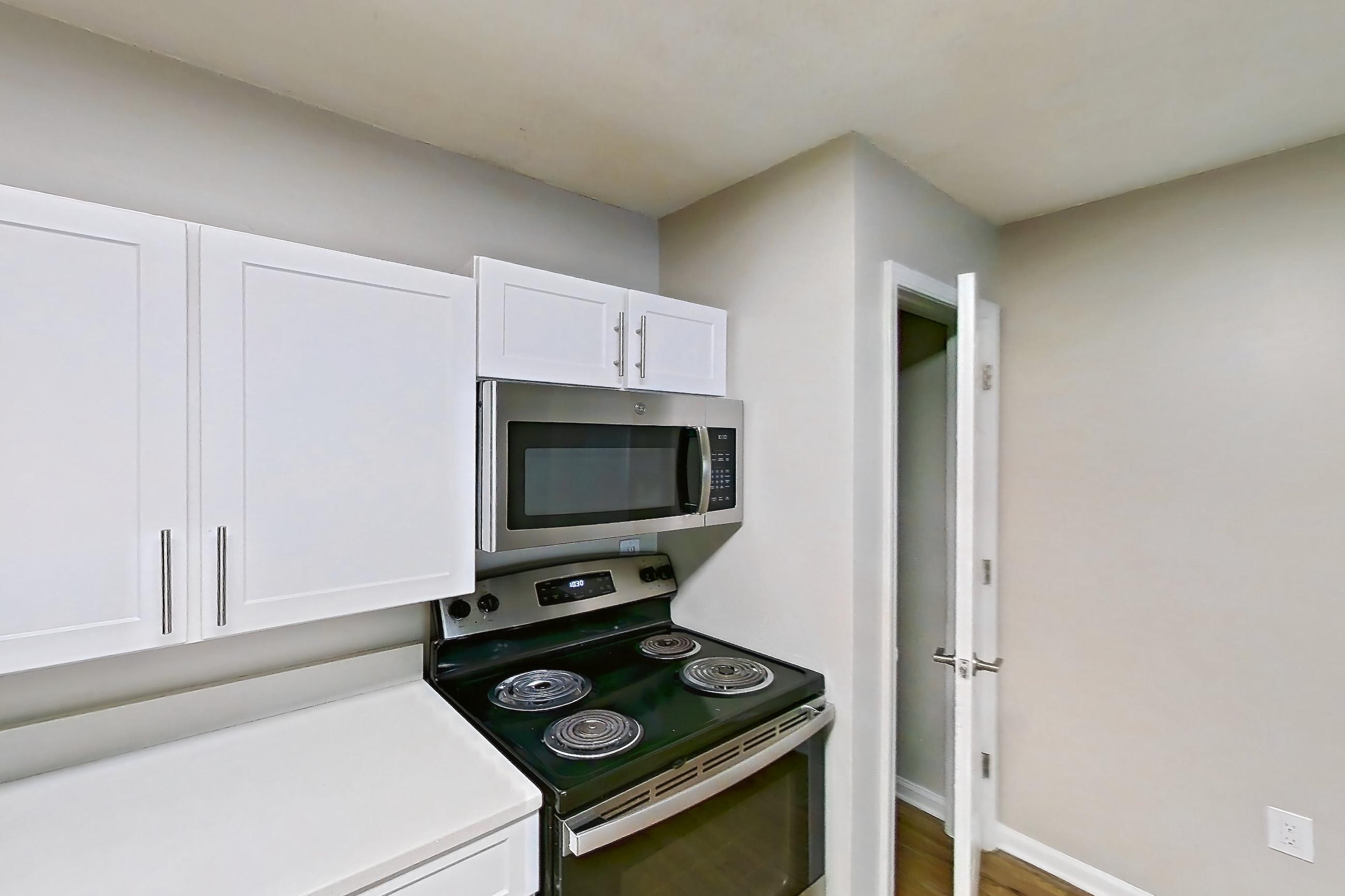 Kitchen with dishwasher, electric range, light countertops, light wood-finish flooring, microwave, oven/range, and stainless steel appliances, Apartment 6800-1C at Ashford Place