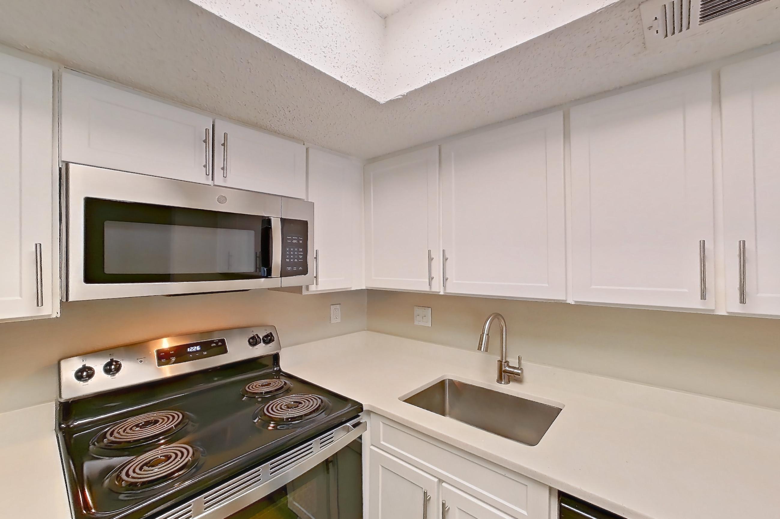Kitchen with dishwasher, electric range, light countertops, light stone countertops, light wood-finish flooring, microwave, oven/range, refrigerator, and stainless steel appliances, Apartment 0618 at Beacon Hill