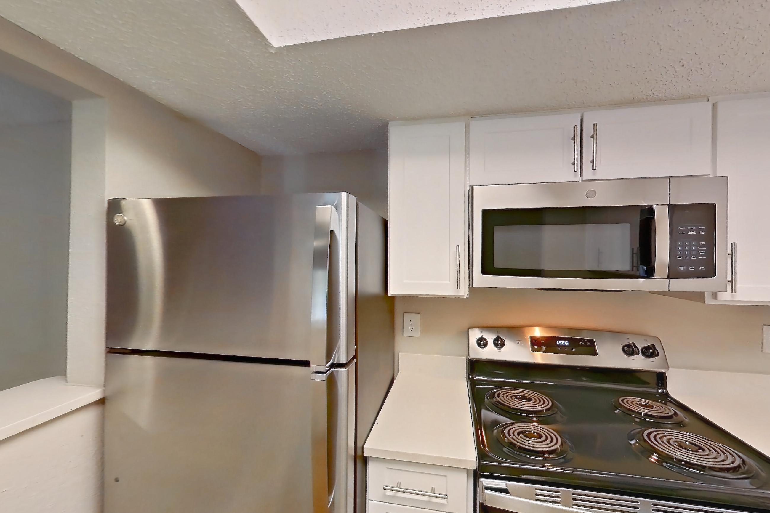 Kitchen with dishwasher, electric range, light countertops, light stone countertops, light wood-finish flooring, microwave, oven/range, refrigerator, and stainless steel appliances, Apartment 0618 at Beacon Hill
