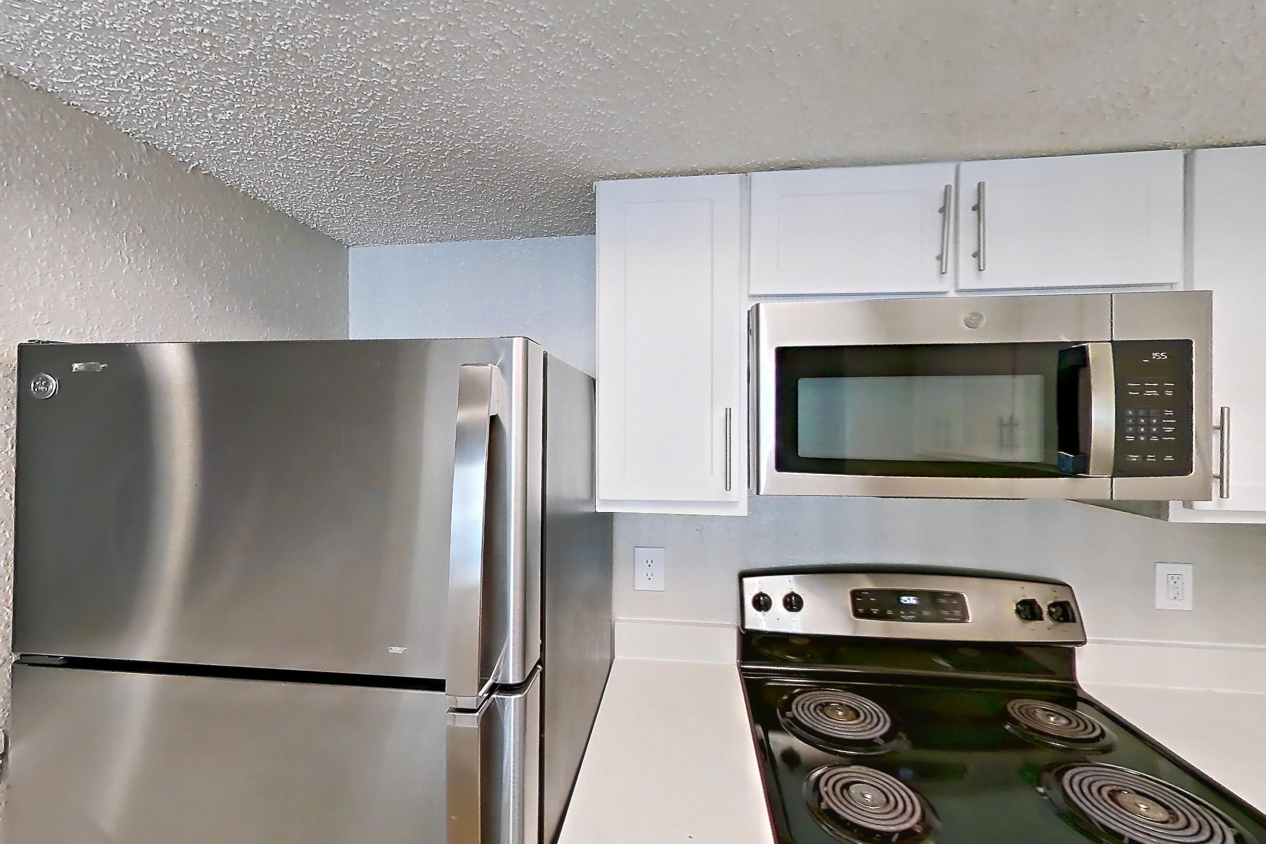 Kitchen with dishwasher, electric range, light countertops, light wood-finish flooring, microwave, oven/range, refrigerator, and stainless steel appliances, Apartment 0414 at Beacon Hill