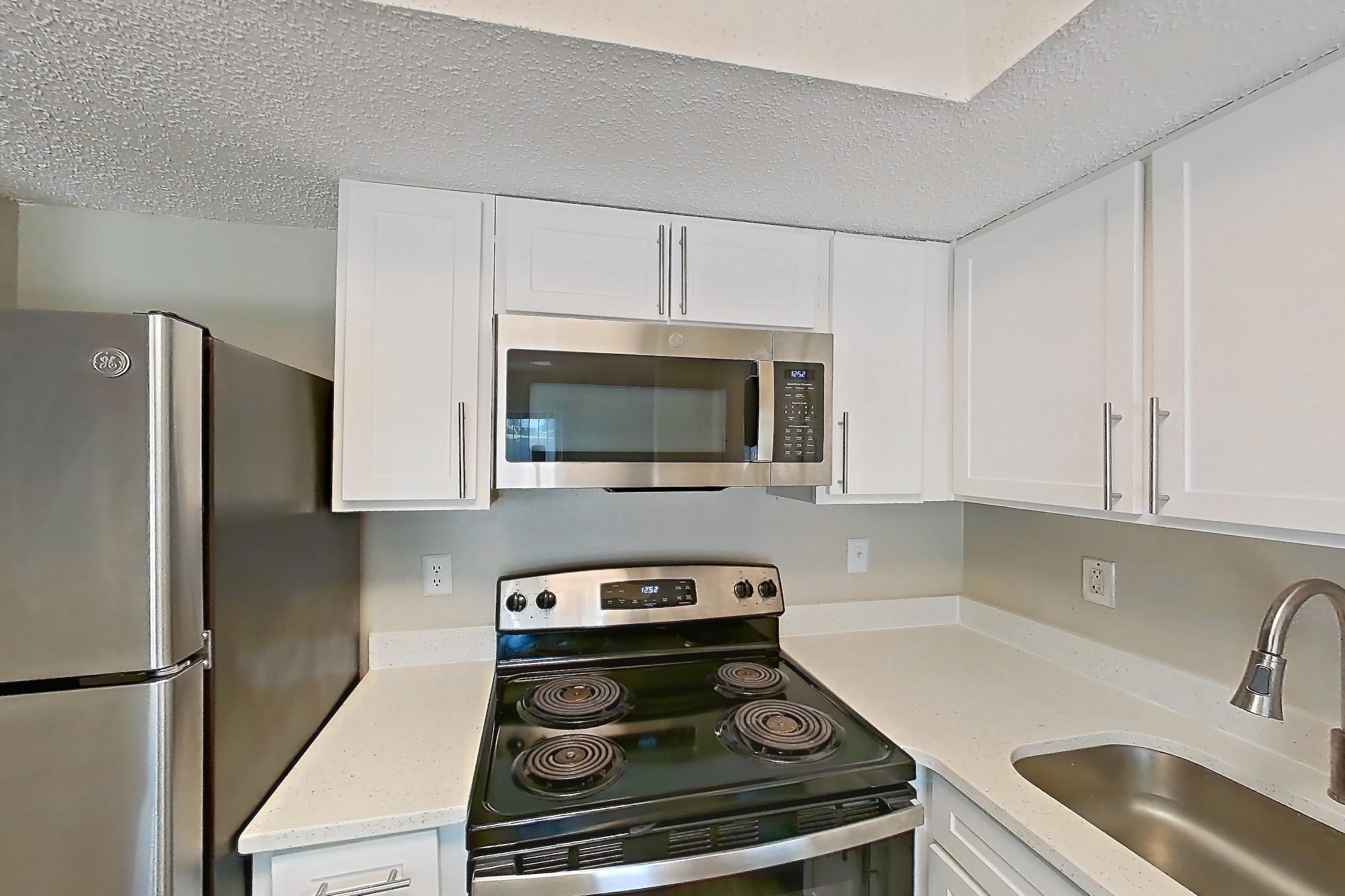 Kitchen with dishwasher, electric range, light countertops, light stone countertops, light wood-finish flooring, microwave, oven/range, range hood, refrigerator, and stainless steel appliances, Apartment 1102 at Beacon Hill